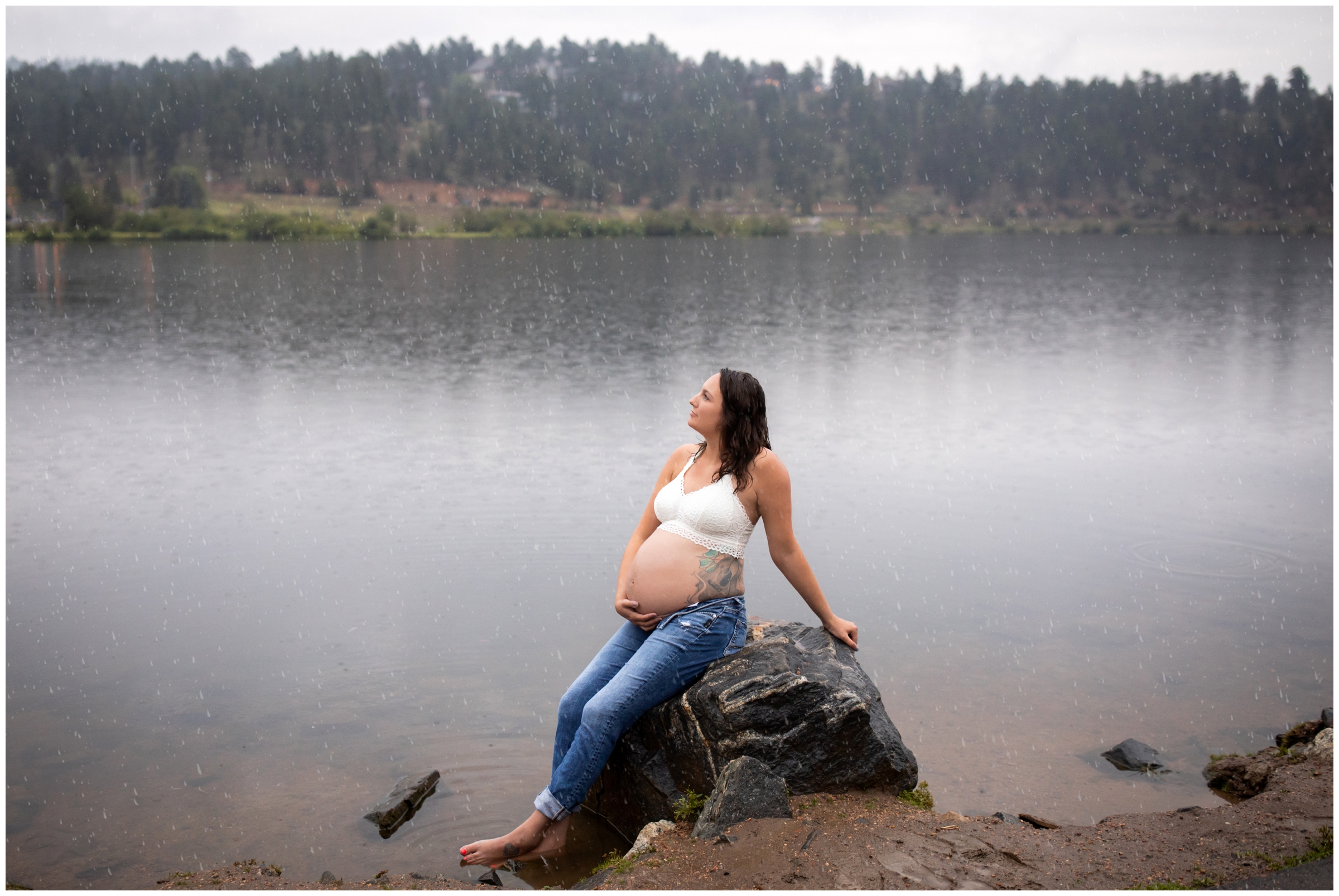 pregnant woman posing in front of lake in the rain during Evergreen Colorado maternity photos