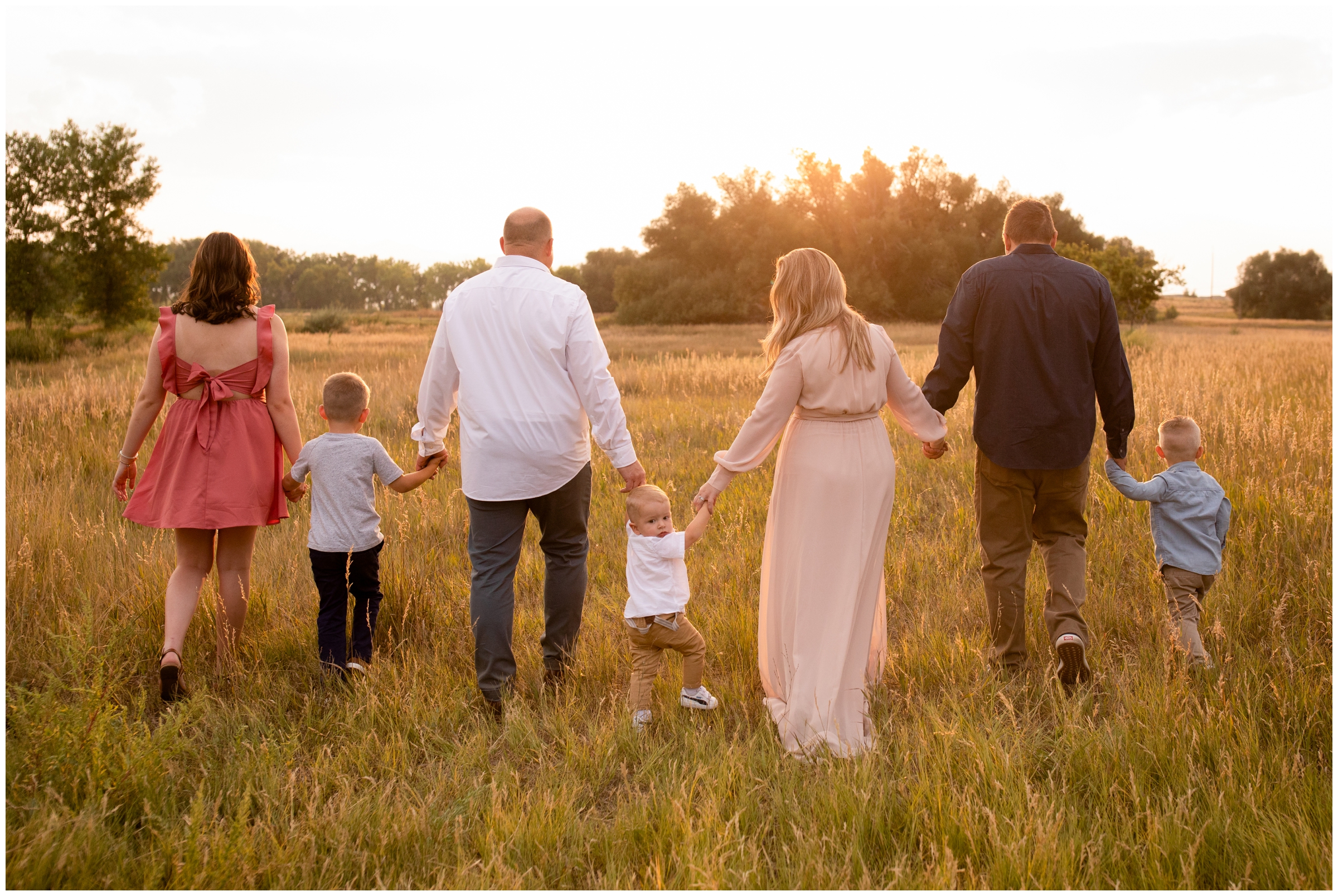 family holding hands and walking through a field during sunny family photos in Longmont Colorado