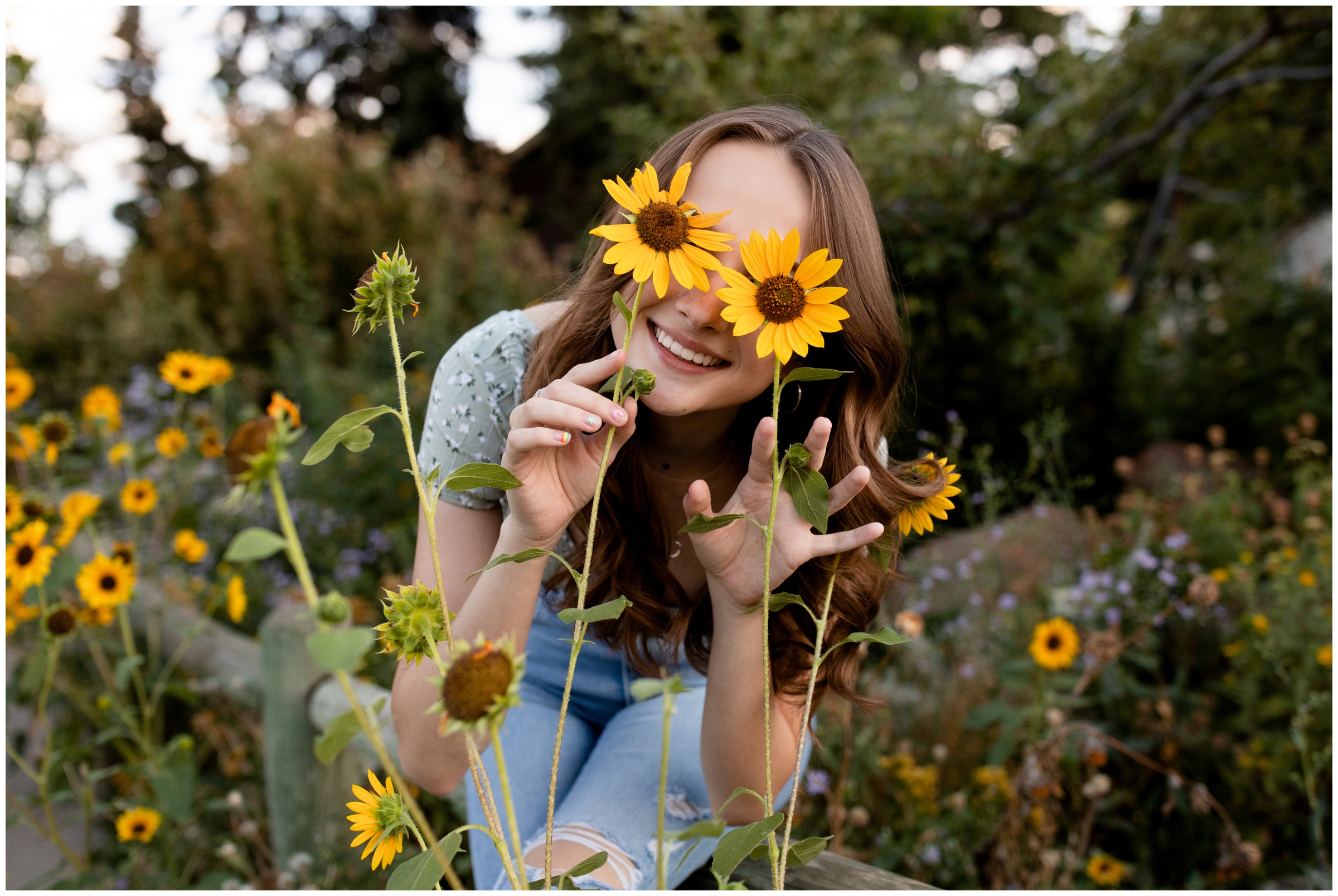 teen covering eyes with sunflowers during Colorado summer senior photography session by Plum Pretty Photos