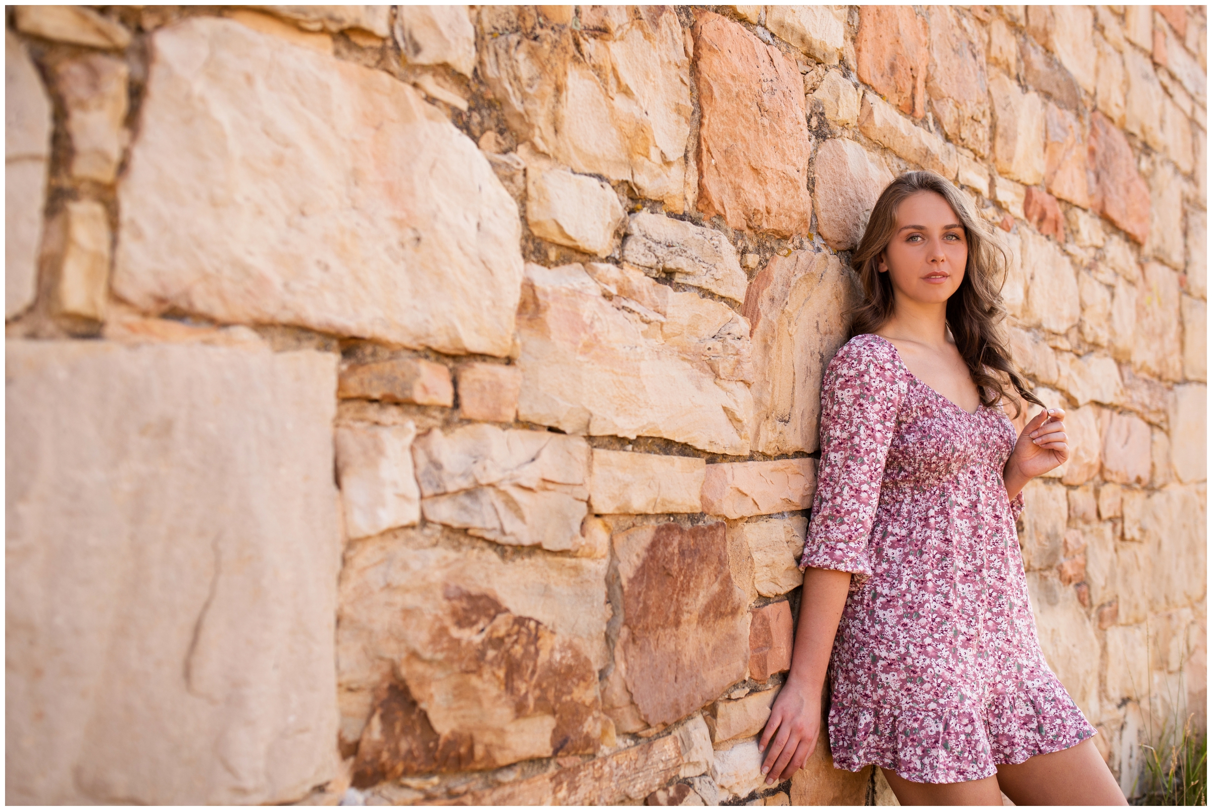 teen girl leaning against stone wall during Boulder Colorado senior photos at South Mesa Trail