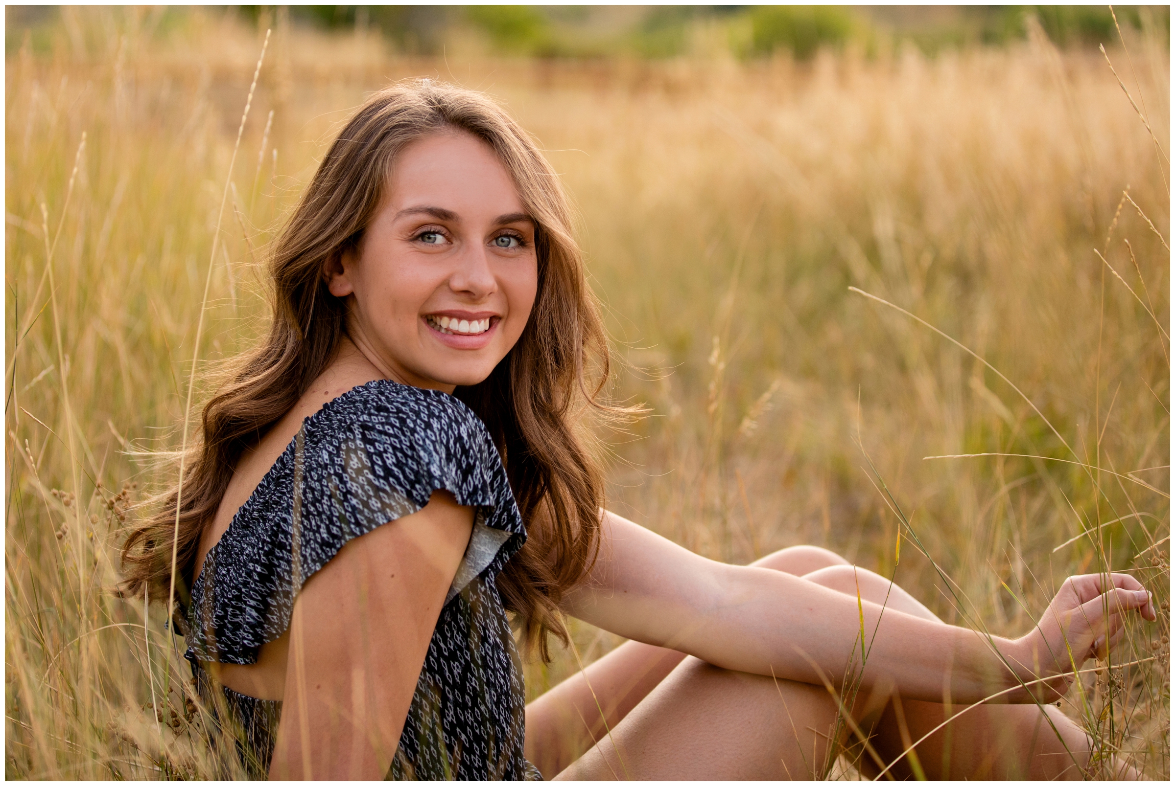 teen girl sitting in field of long grasses during Boulder senior photos at South Mesa