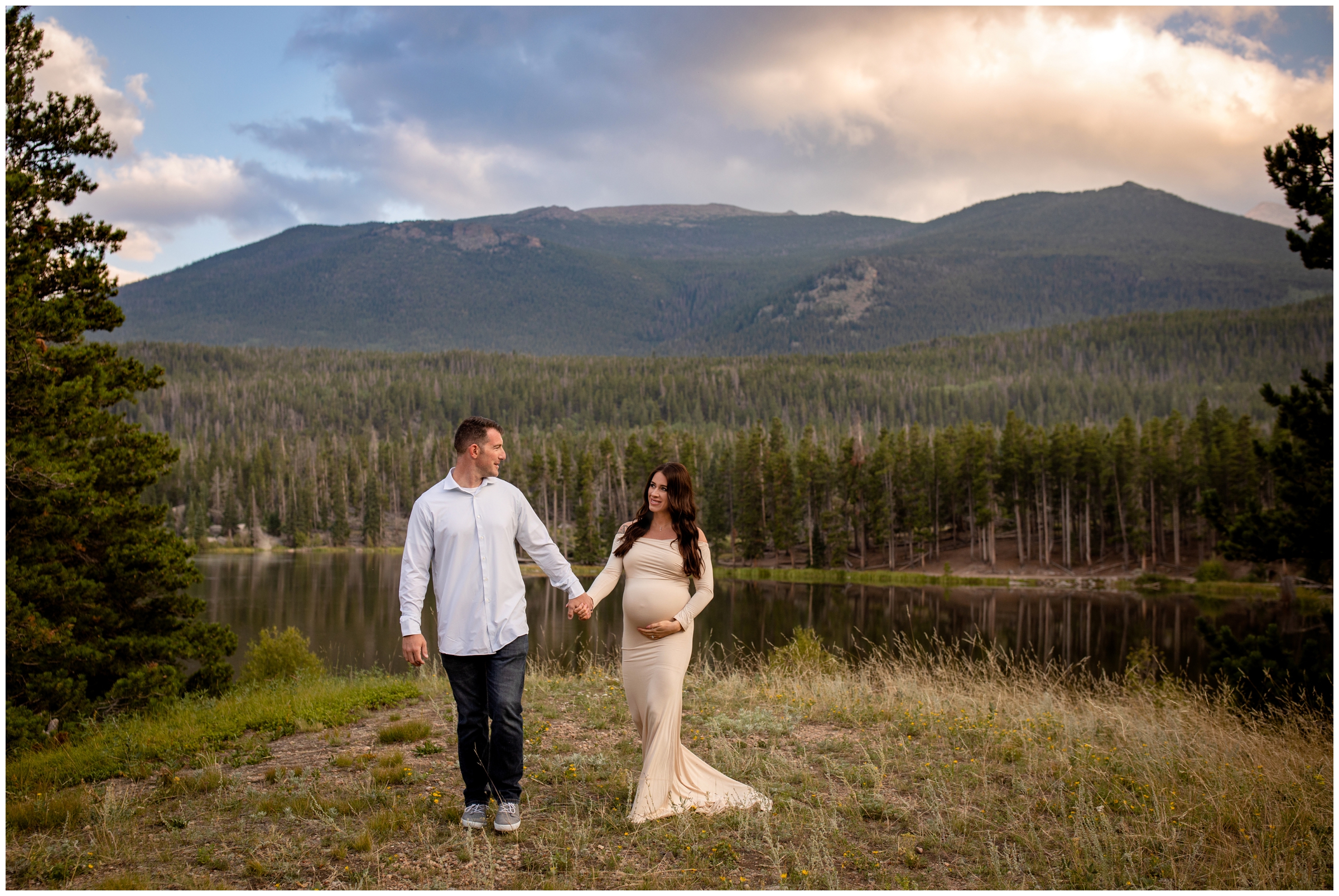 couple walking through a field with mountains in background during Estes Park Colorado maternity portraits in RMNP