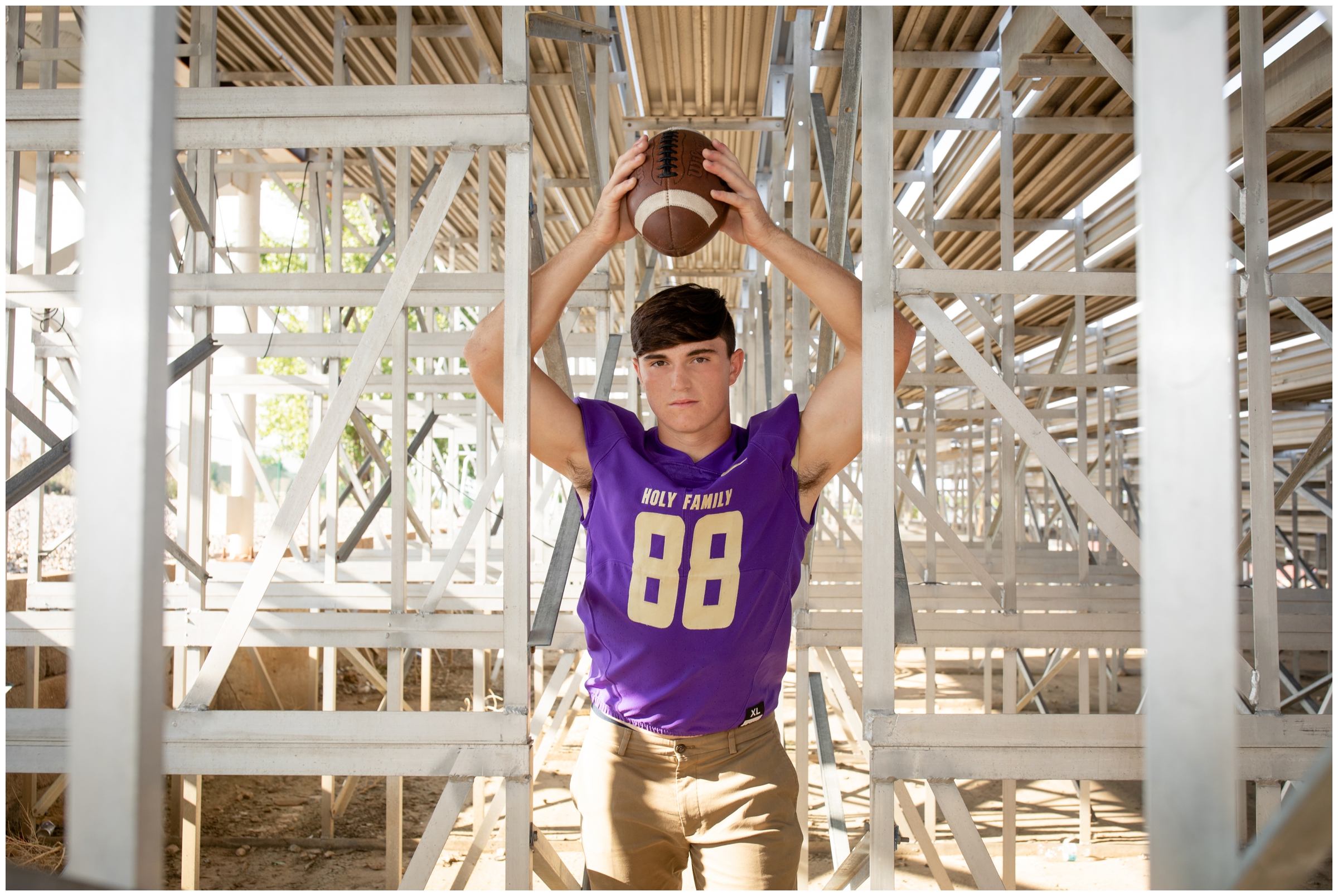 teen football player posing under bleachers during Holy Family High school senior photos in Colorado