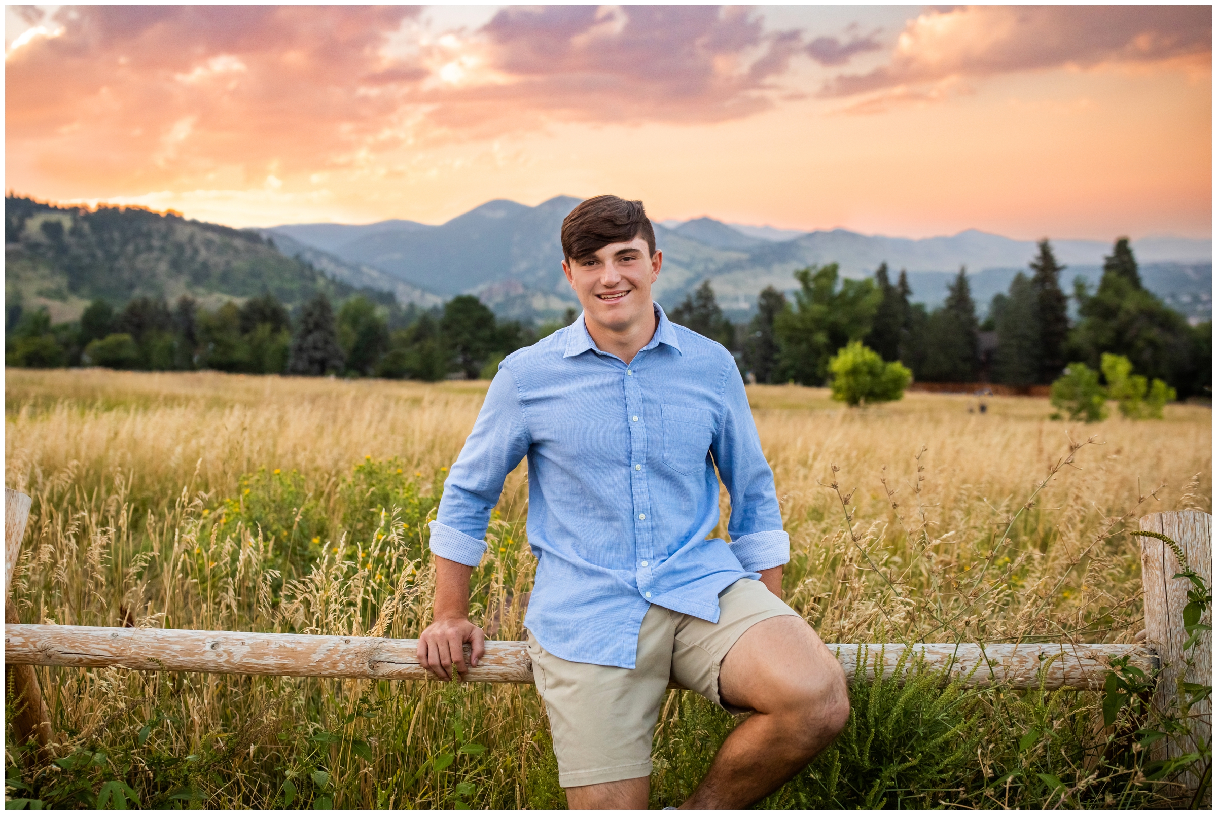 senior guy leaning on fence during Holy Family Colorado senior pictures at sunset