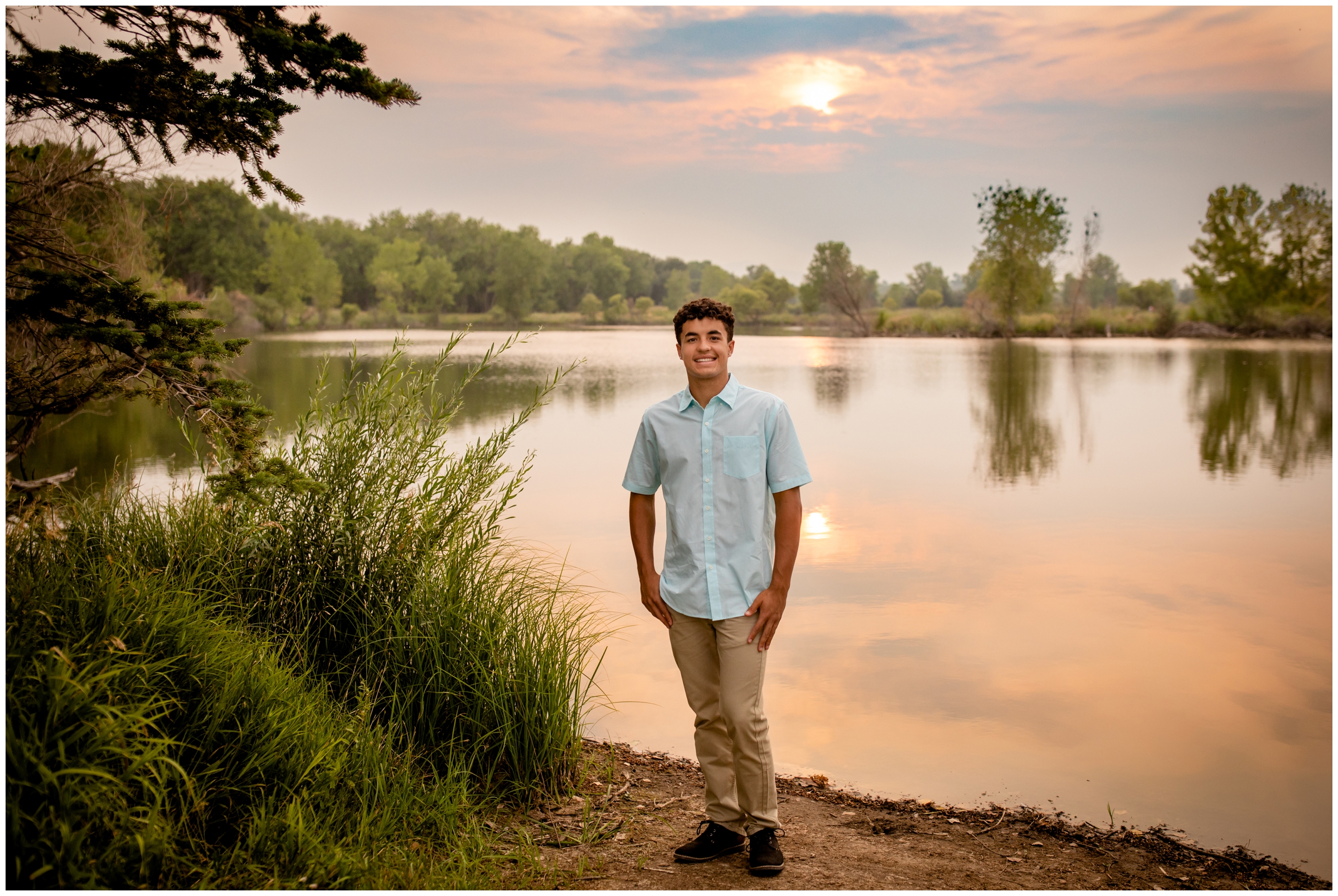 teen boy standing next to a lake at sunset during Longmont High school senior pictures 