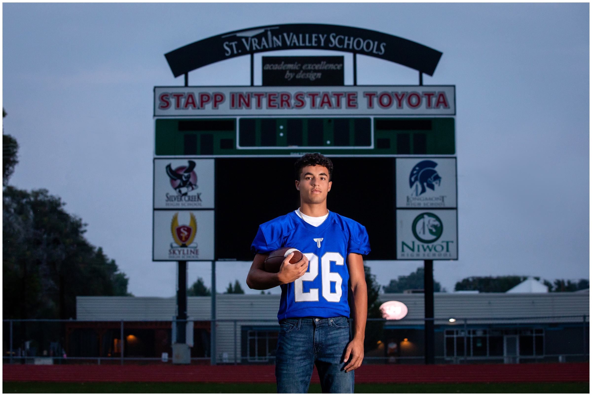 teen football player posing in front of scoreboard during Longmont High School senior pictures 