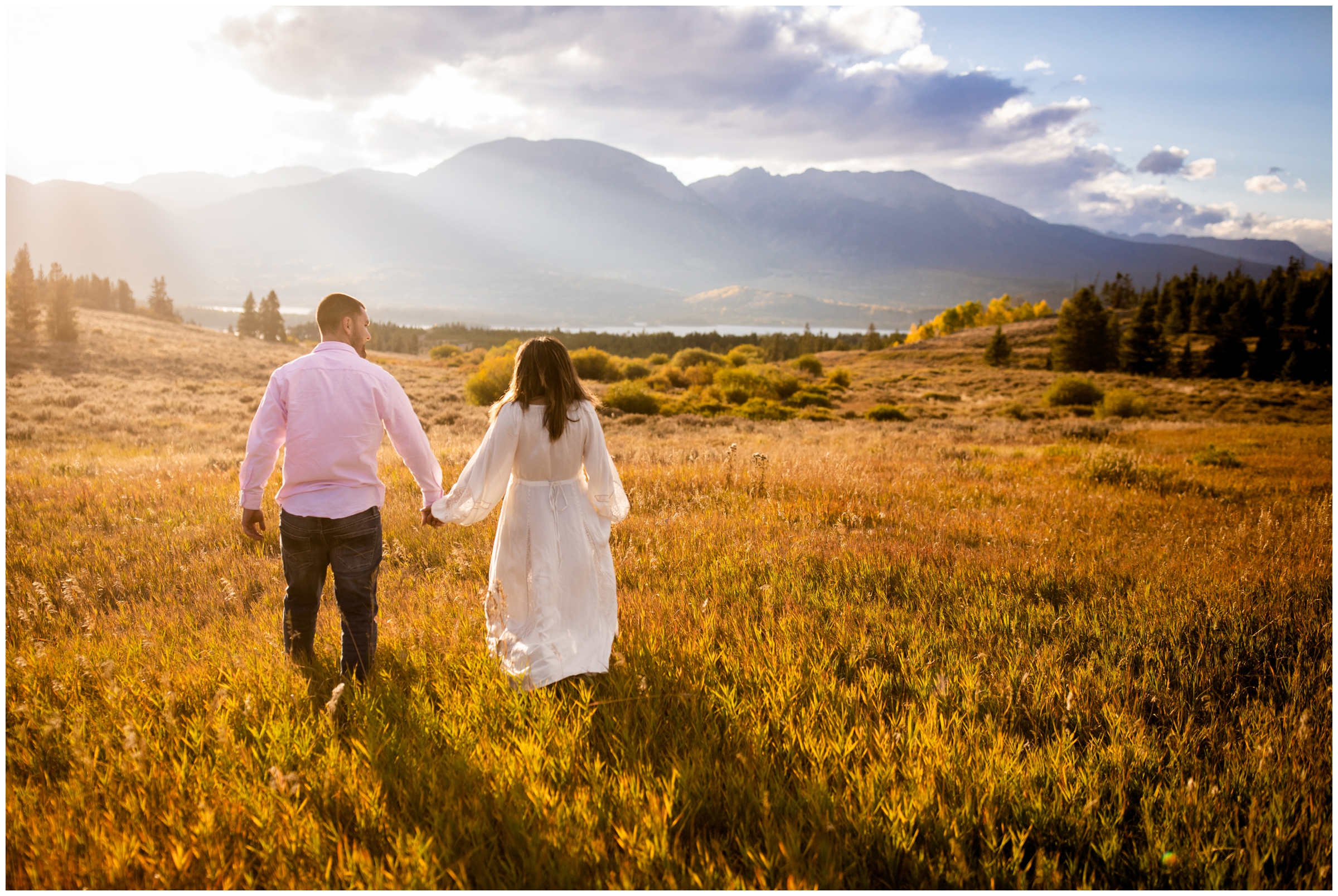 couple holding hands and walking through a field at windy point campground in summit county Colorado 