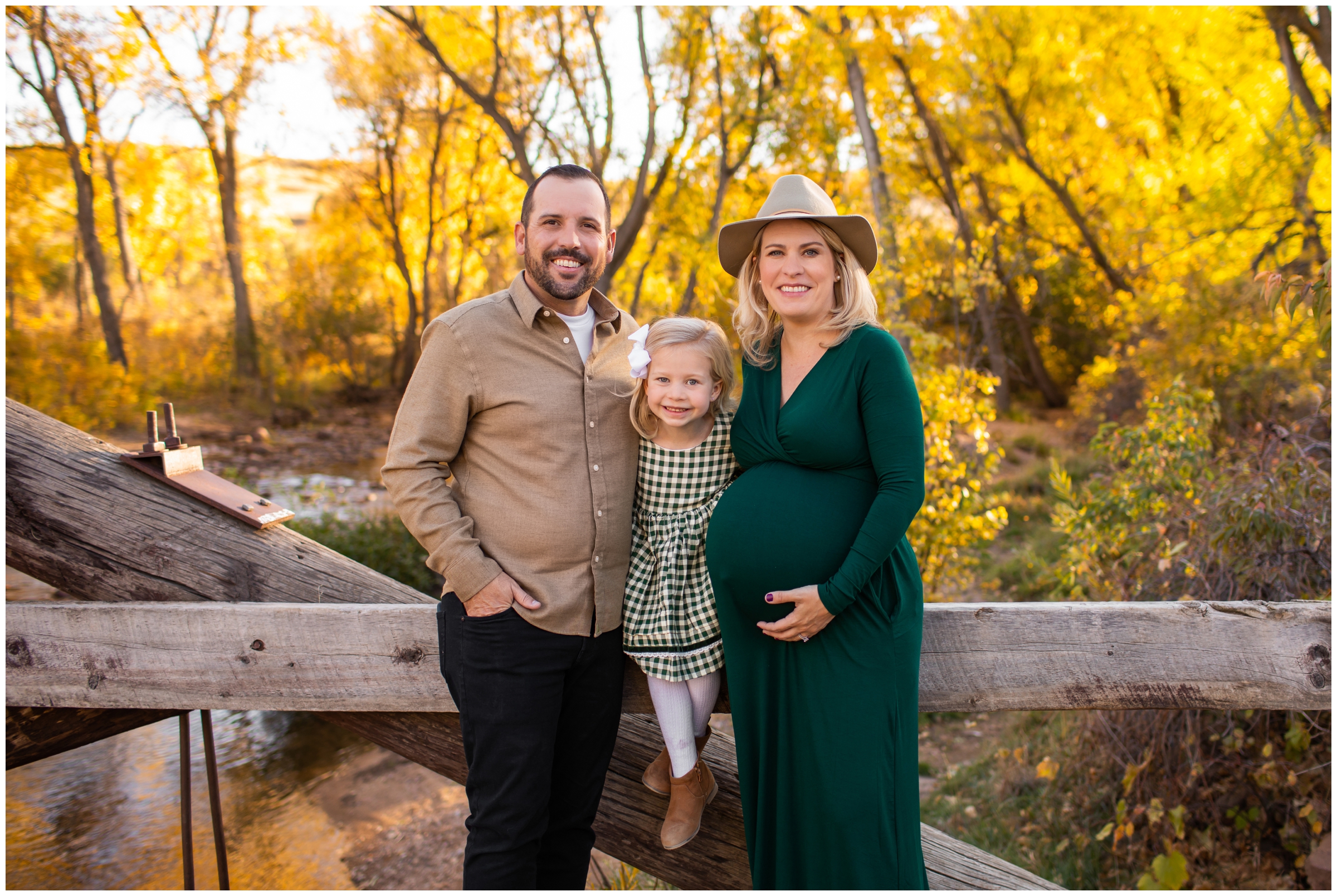 family of three posing on wooden bridge during Boulder Colorado maternity family photo session during fall 