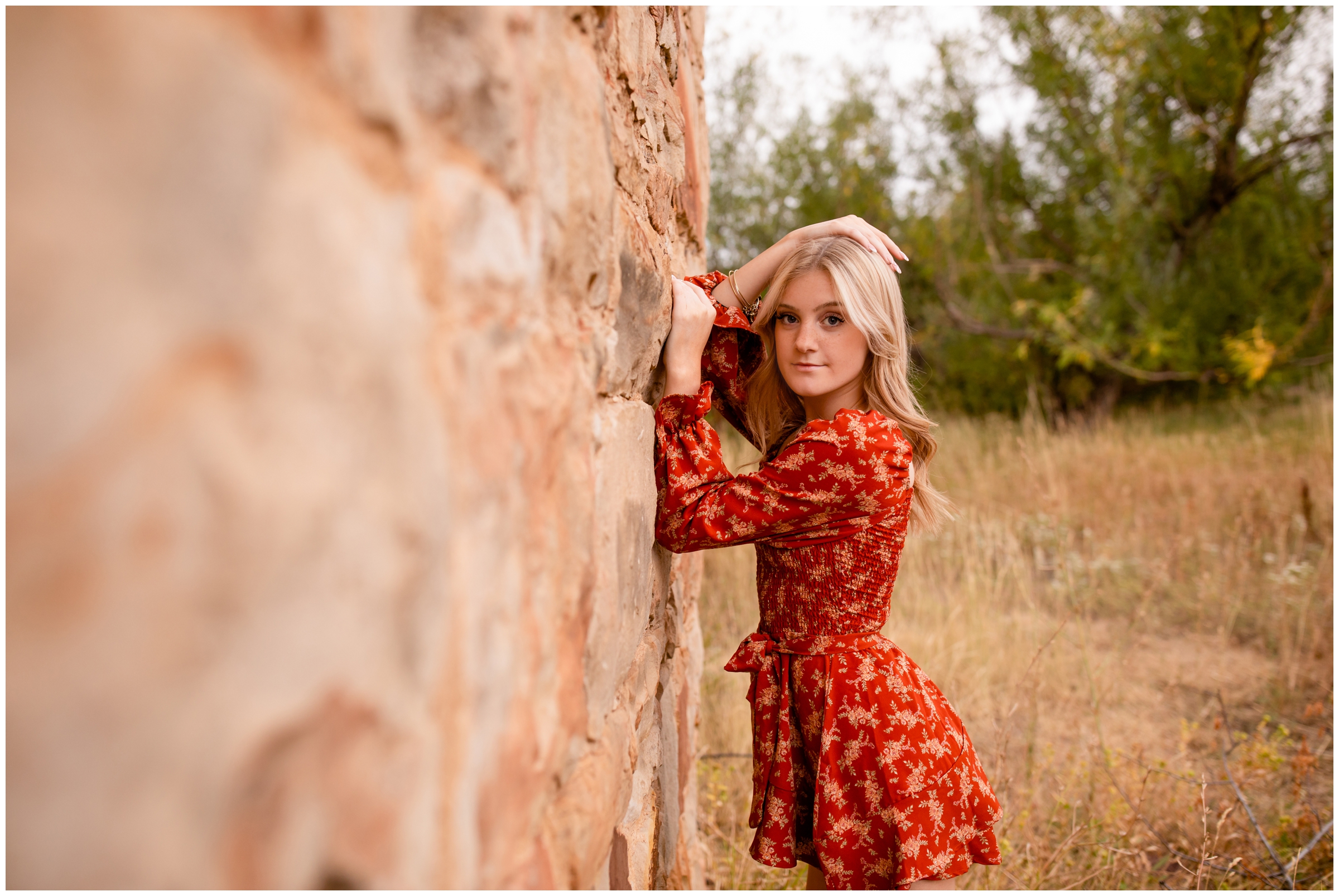 teen leaning against stone wall during fall senior pictures at South Mesa Trail in Colorado 