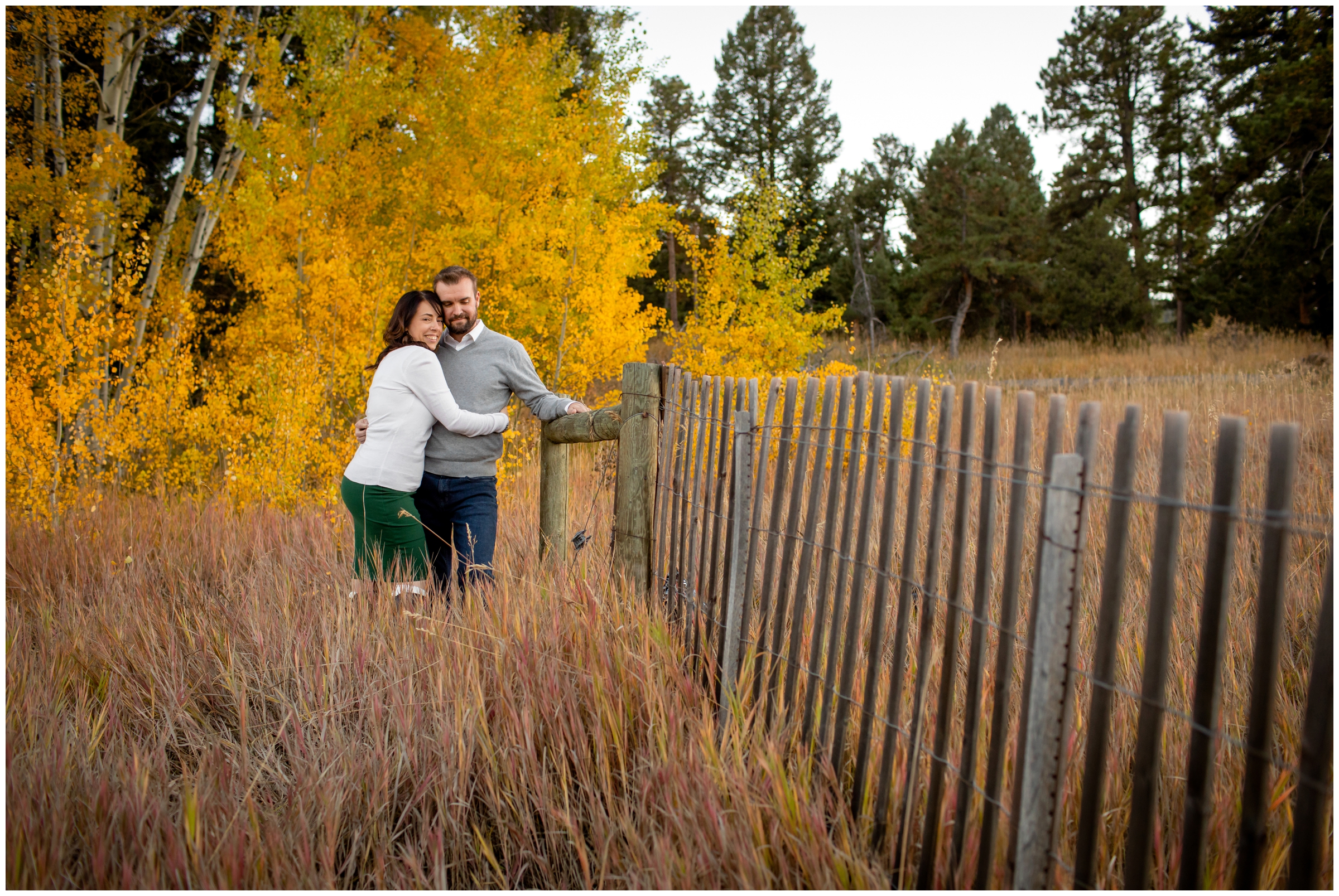 couple cuddling by rustic wooden fence during Morrison Colorado engagement pictures 