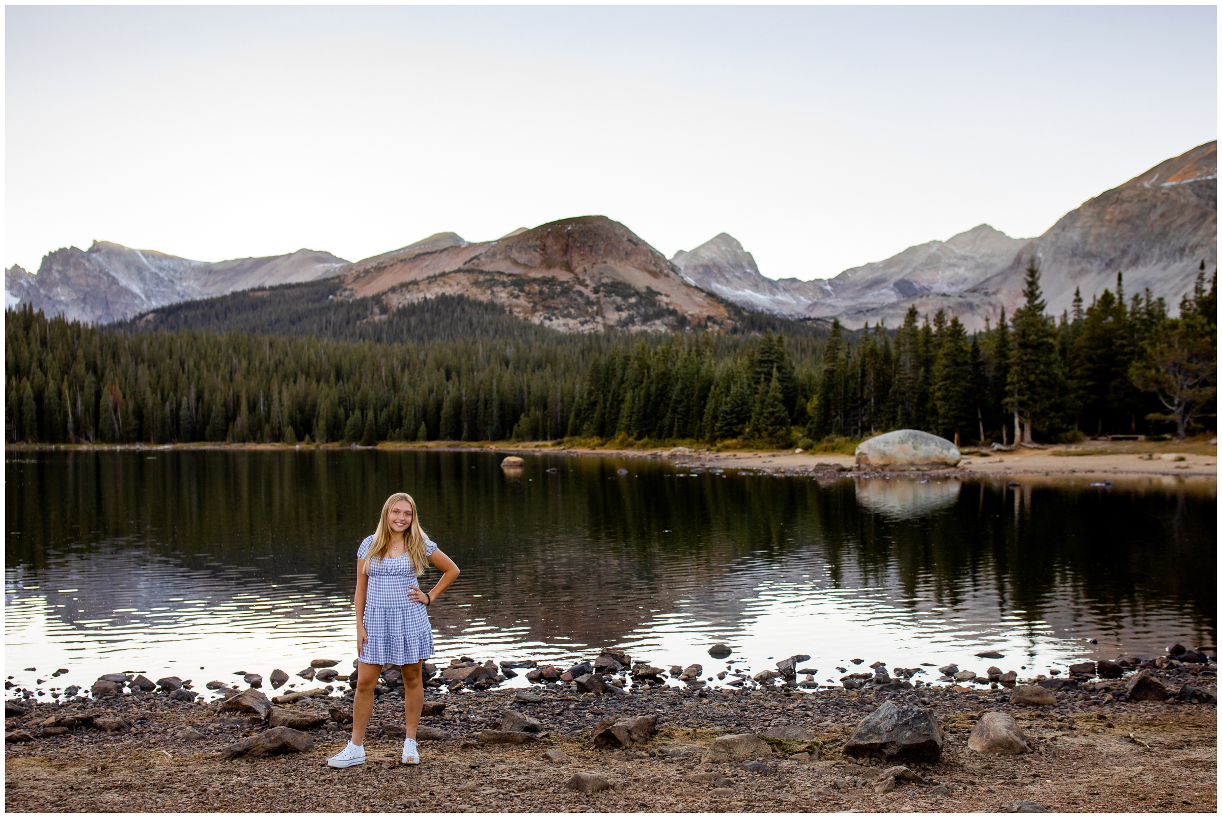 teen in gingham dress posing in front of mountain lake for senior pictures in Colorado mountains 