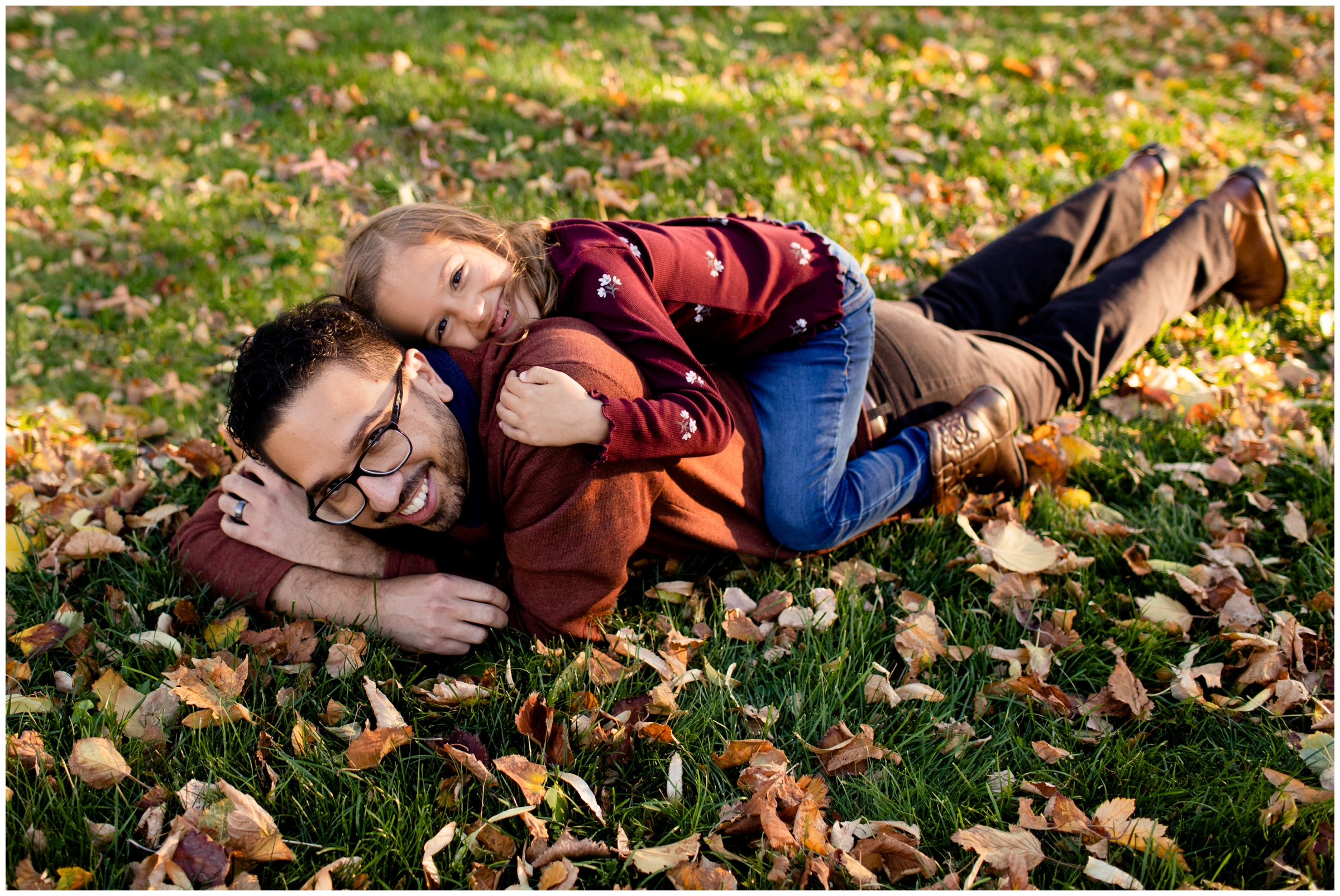 little girl laying on dad's back in the leaves during Colorado fall family photos at Cheesman Park
