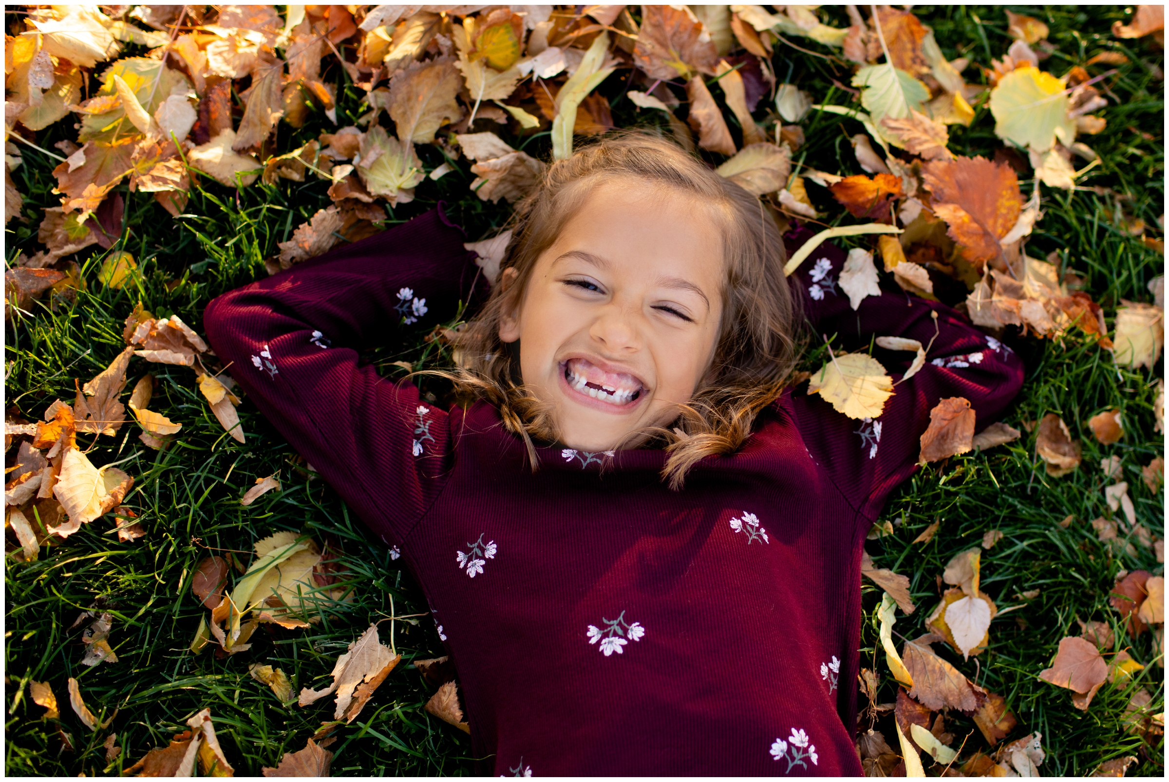 little girl laying in the leaves during fall Colorado family photos at Cheesman Park Denver