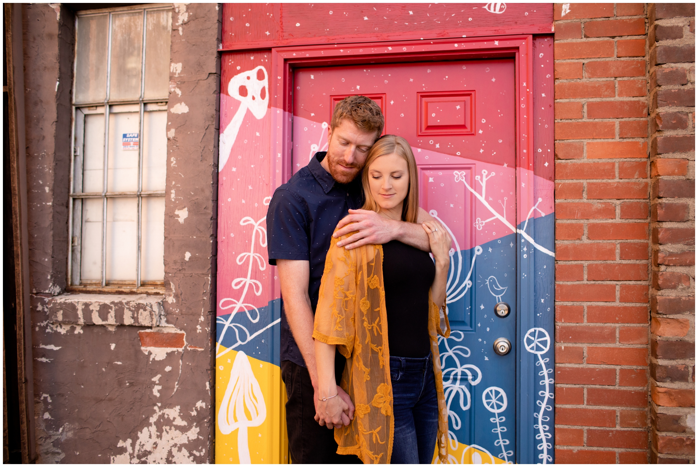 couple cuddling in front of colorfully painted door in Old Town Fort Collins during Colorado engagement photography session 