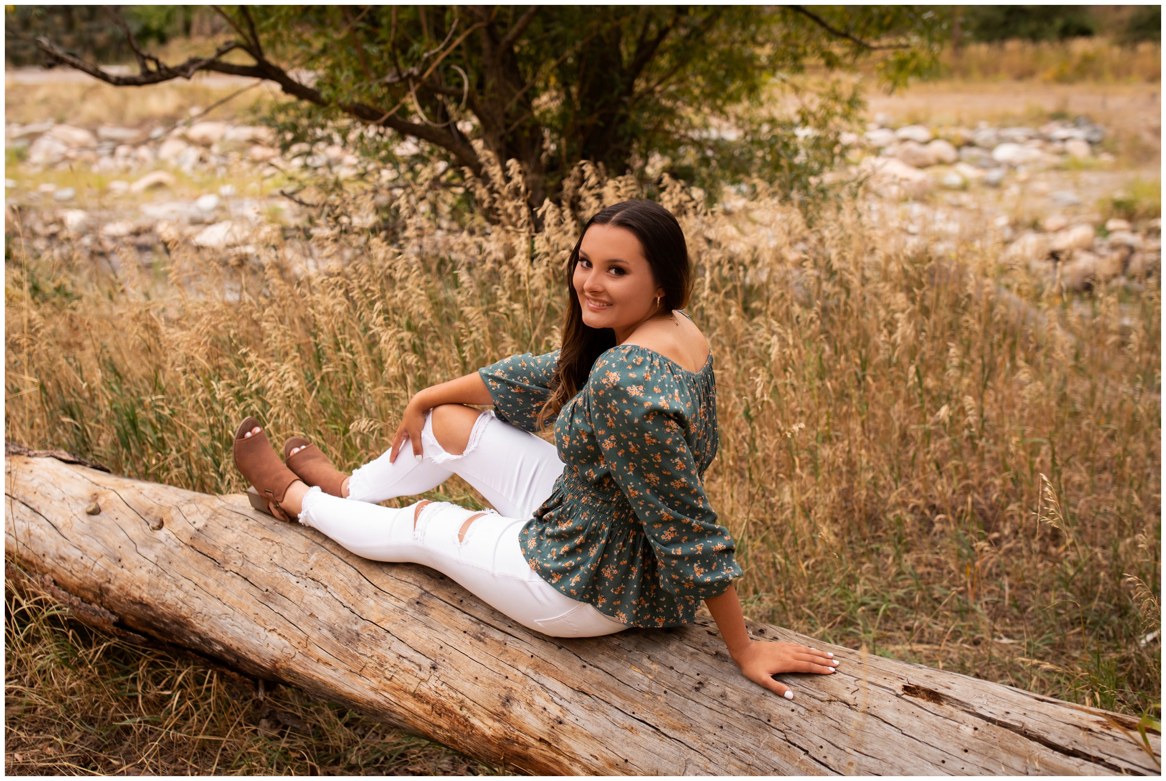 teen girl sitting on downed tree trunk during colorado graduation portraits in the mountains
