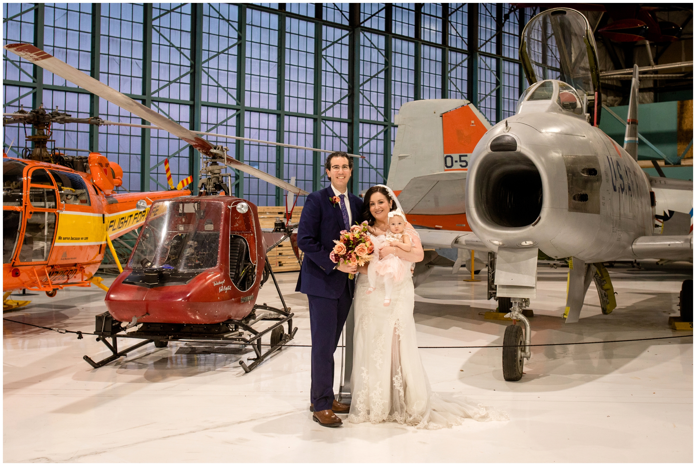 bride and groom and baby daughter flower girl posing in front of vintage planes at Denver airplane museum wedding 