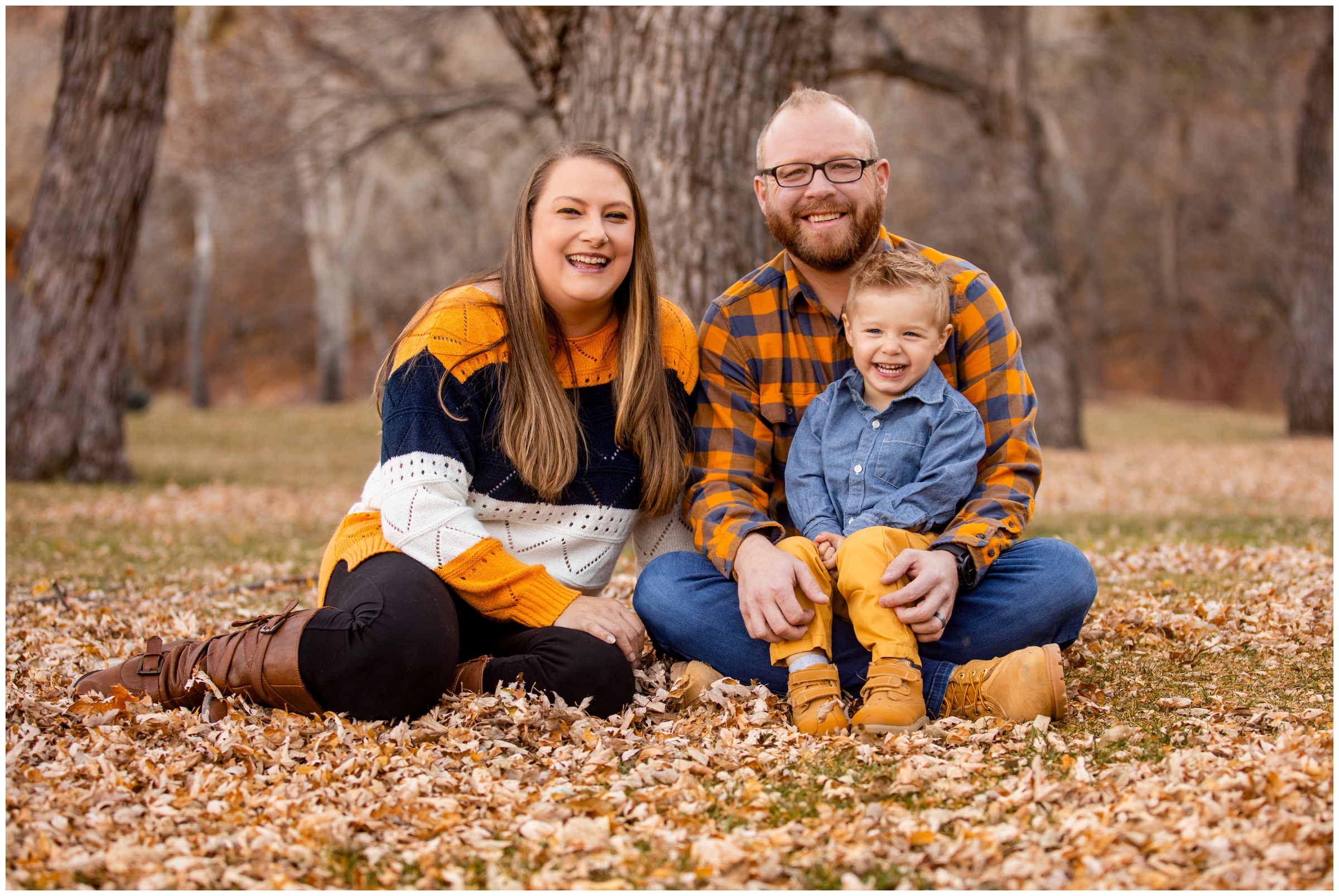 family of three sitting in a pile of leaves during Lyons Colorado fall family mini session by Plum Pretty Photography