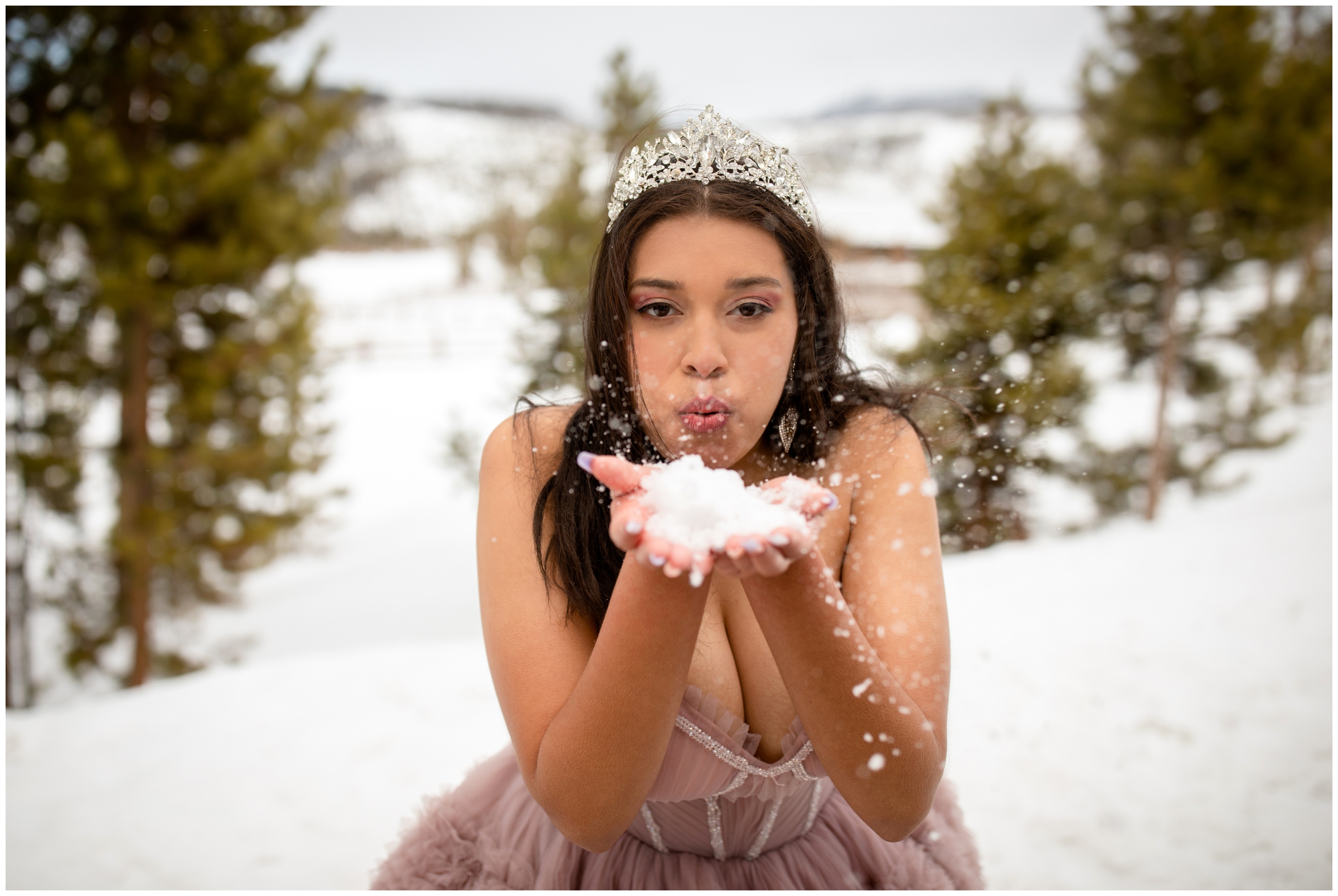 teen blowing snow at the camera during winter senior portraits in the Colorado mountains near Winter Park 