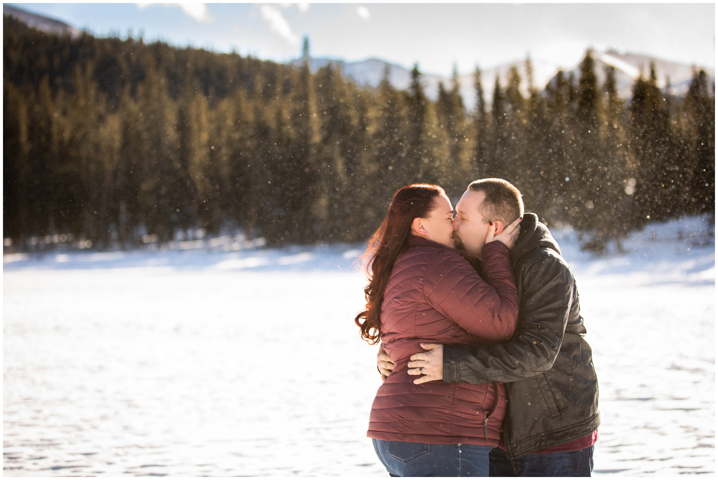 couple kissing while standing on frozen mountain lake in Colorado during winter engagement pictures