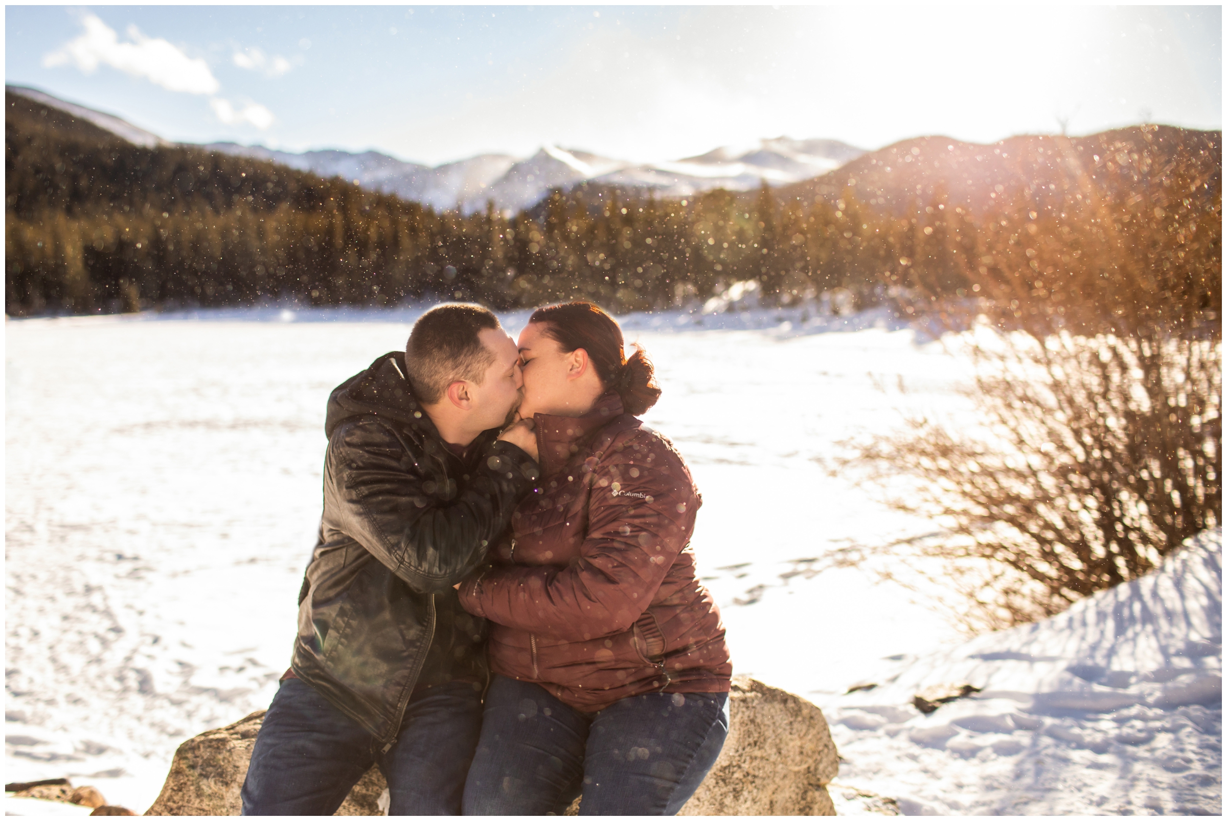 couple kissing in the snow with mountains in background during Colorado winter engagement pictures 