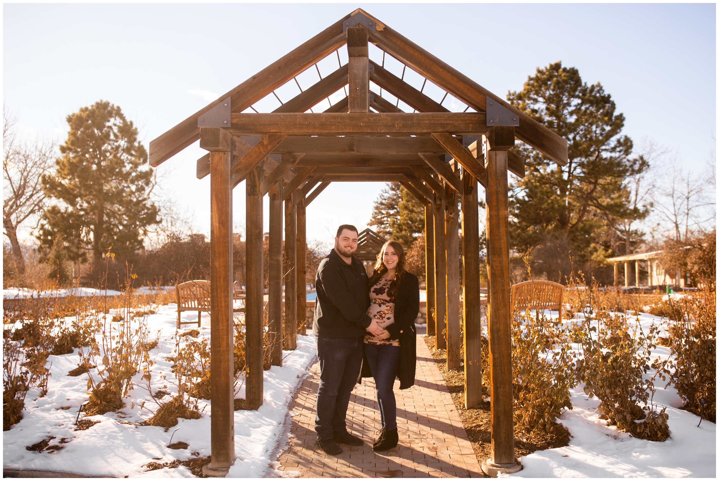 couple posing under wooden arbor at Hudson Gardens during Denver pregnancy photo session