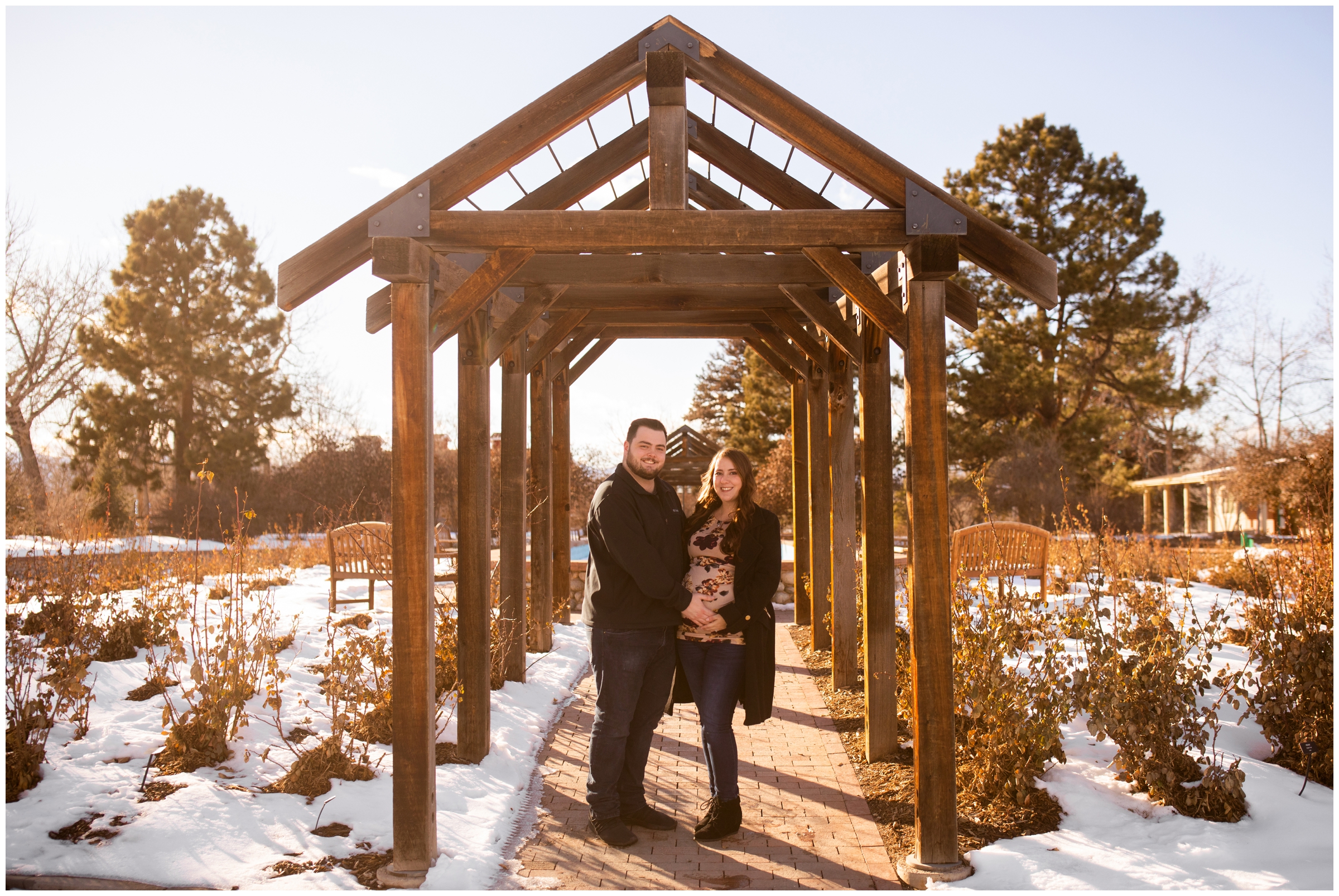 couple posing under wooden arbor at Hudson Gardens during Denver pregnancy photo session 