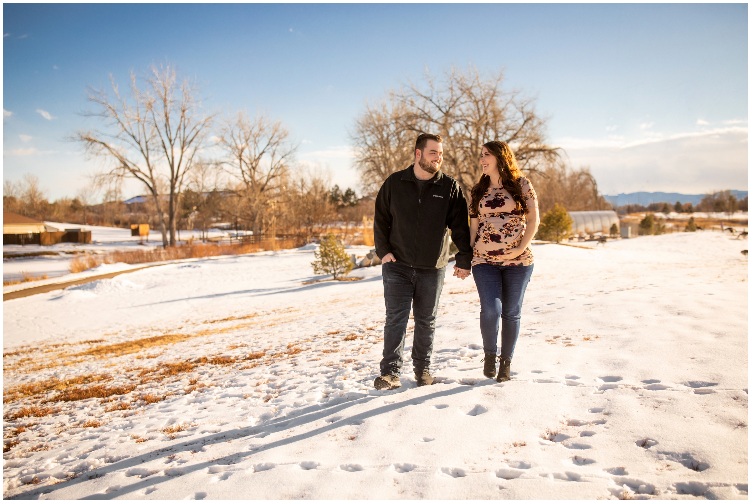 couple holding hands and walking in the snow during Colorado winter maternity pictures at Hudson Gardens 