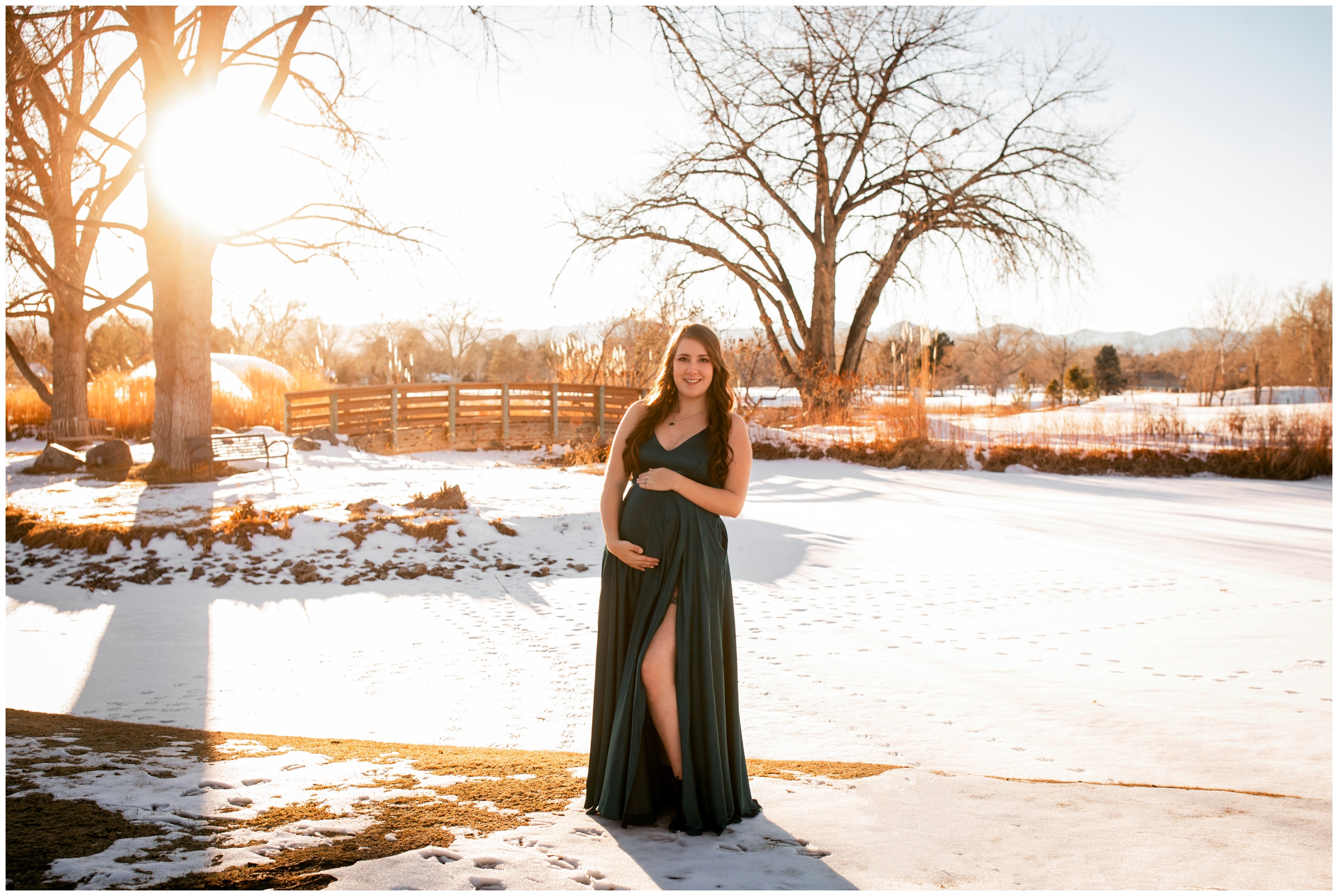 woman posing in the snow in long green dress during Denver pregnancy photo shoot at Hudson Gardens