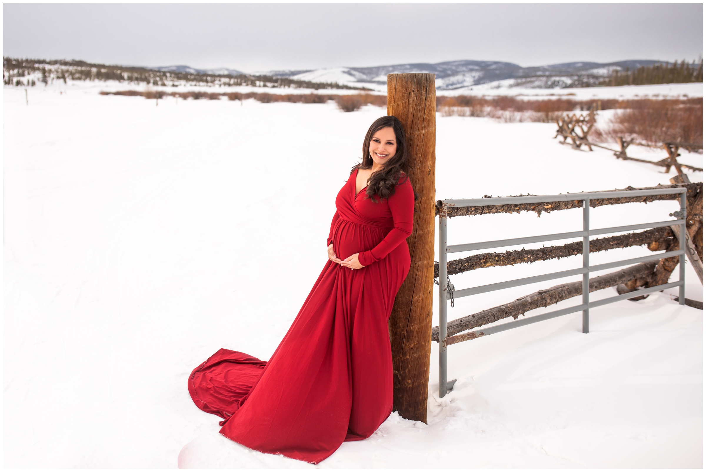 pregnant woman in red dress posing in snow for Winter Park pregnancy photography session 