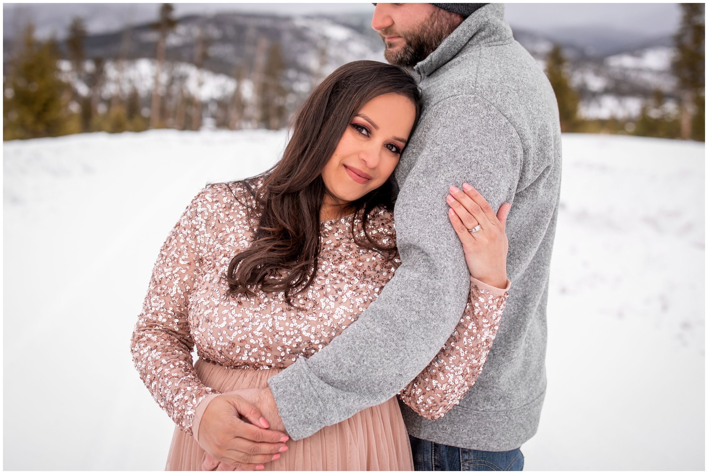 couple cuddling in the snow during Colorado winter maternity pictures in Winter Park 