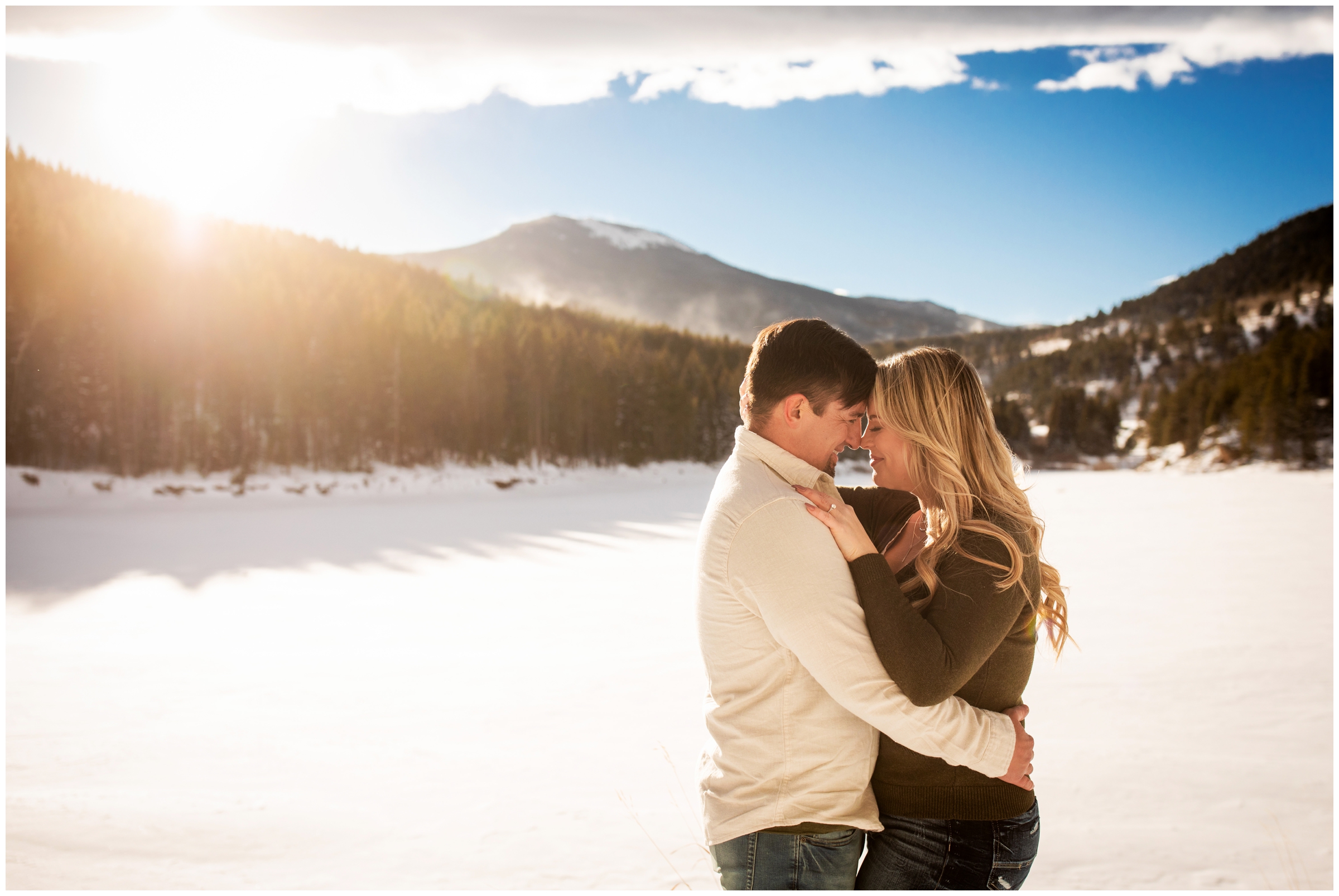 couple cuddling next to a frozen lake in the colorado mountains during Evergreen winter engagement photos 