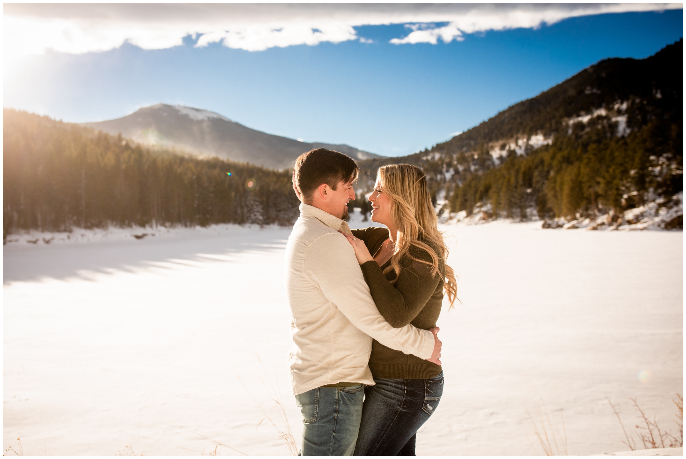 couple cuddling in front of frozen lake during winter engagement pictures in Evergreen Colorado mountains 