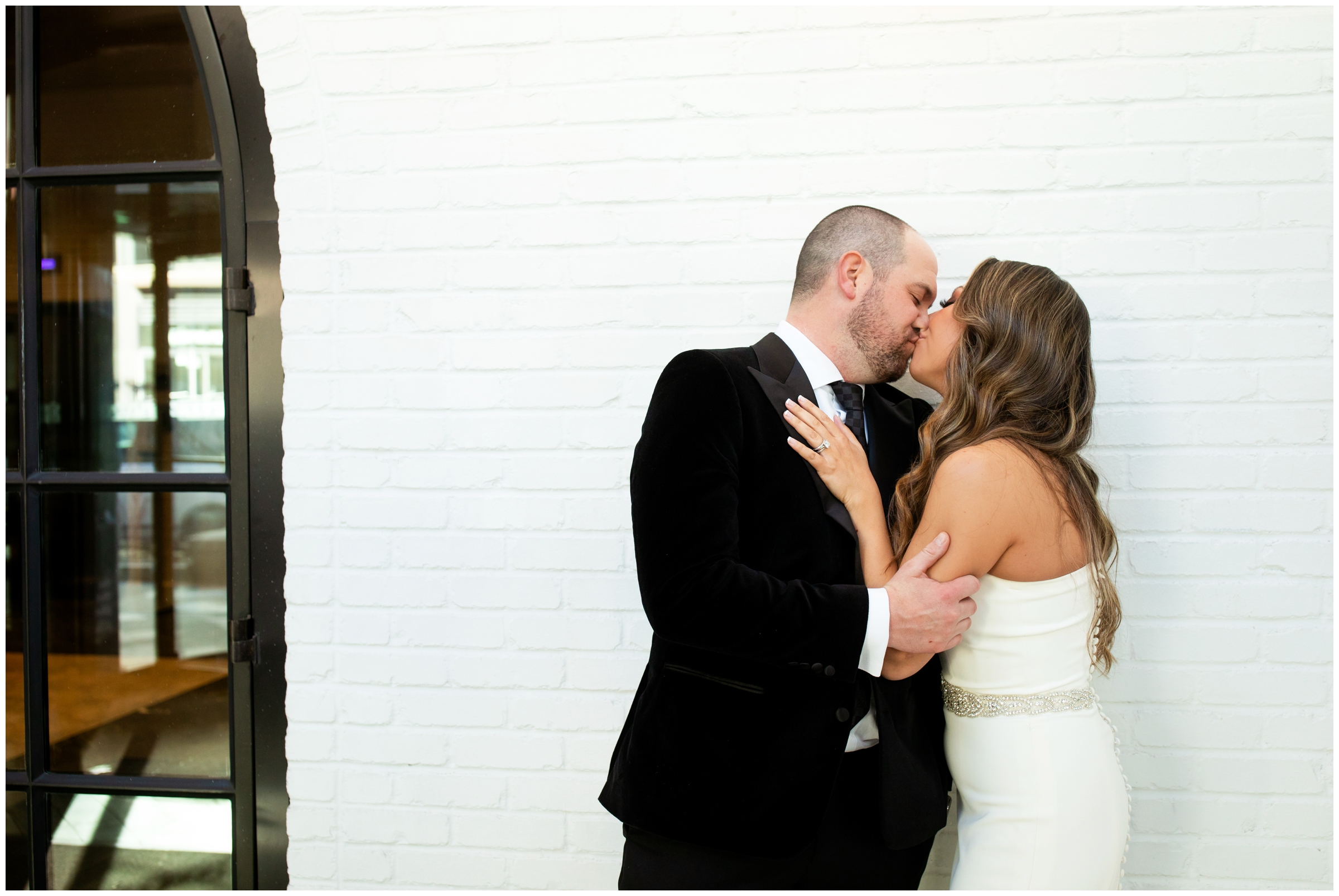 couple kissing in front of white brick wall during urban city wedding at the Halcyon Hotel in Cherry Creek Denver