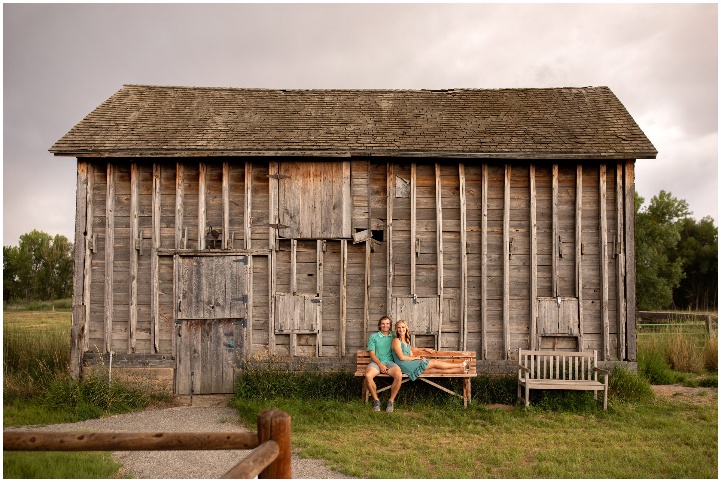couple sitting on a bench in front of a rustic barn at Sandstone Ranch Longmont engagement portraits 