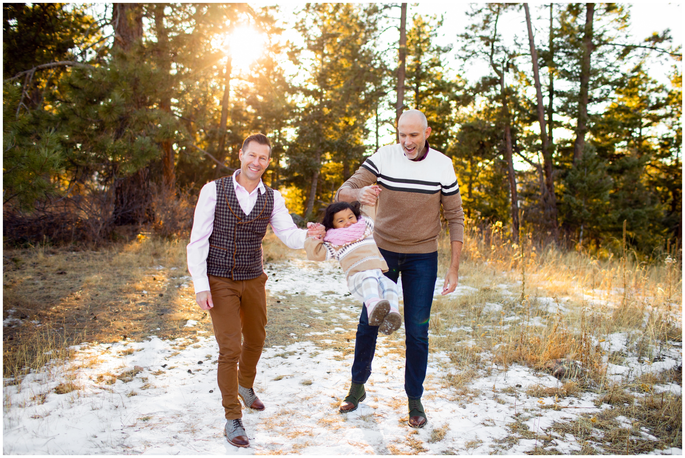 two gay dads swinging daughter during Colorado winter family pictures at Mount Falcon West