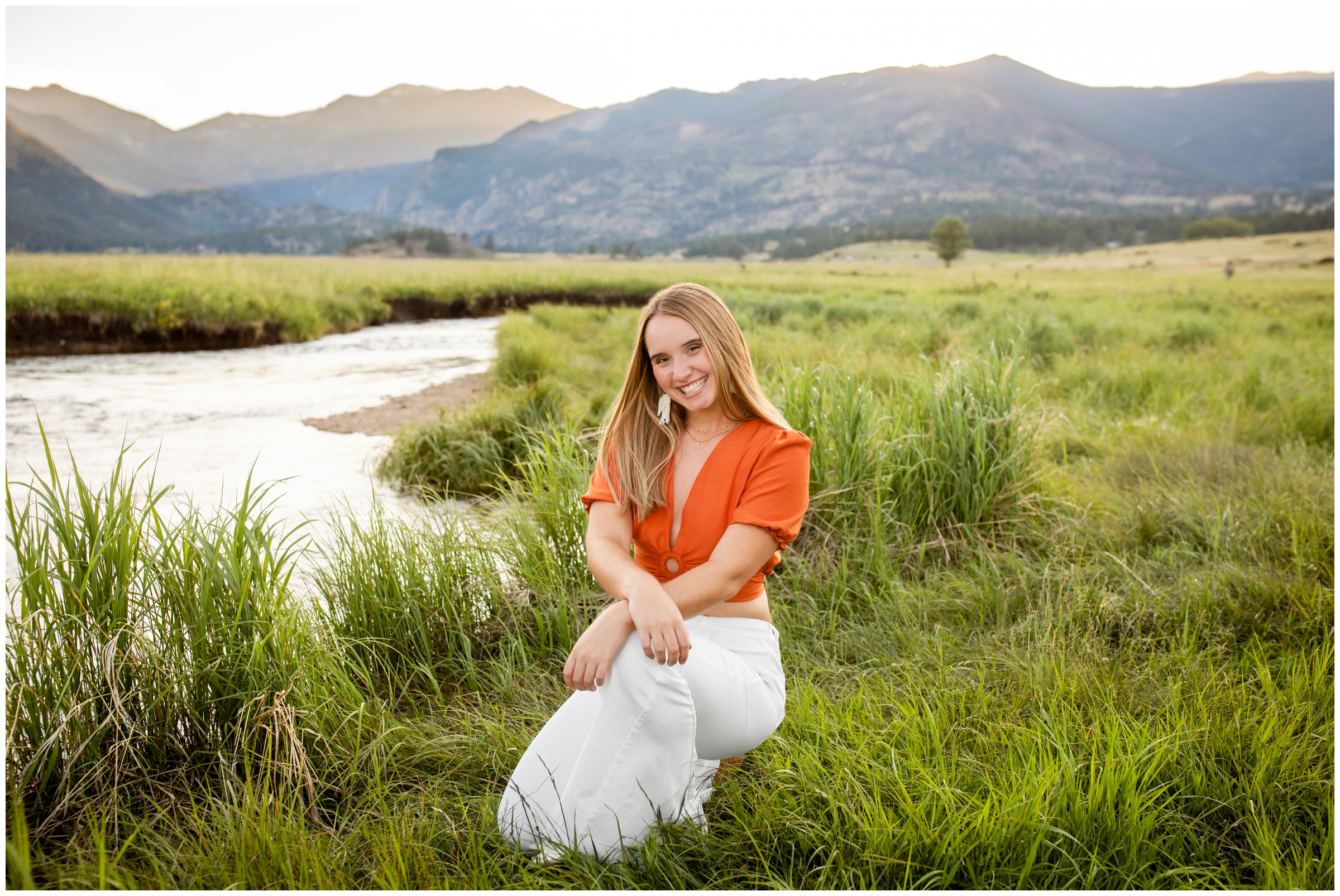 teen kneeling in grass next to a river during mountain senior pictures in Estes Park Colorado 