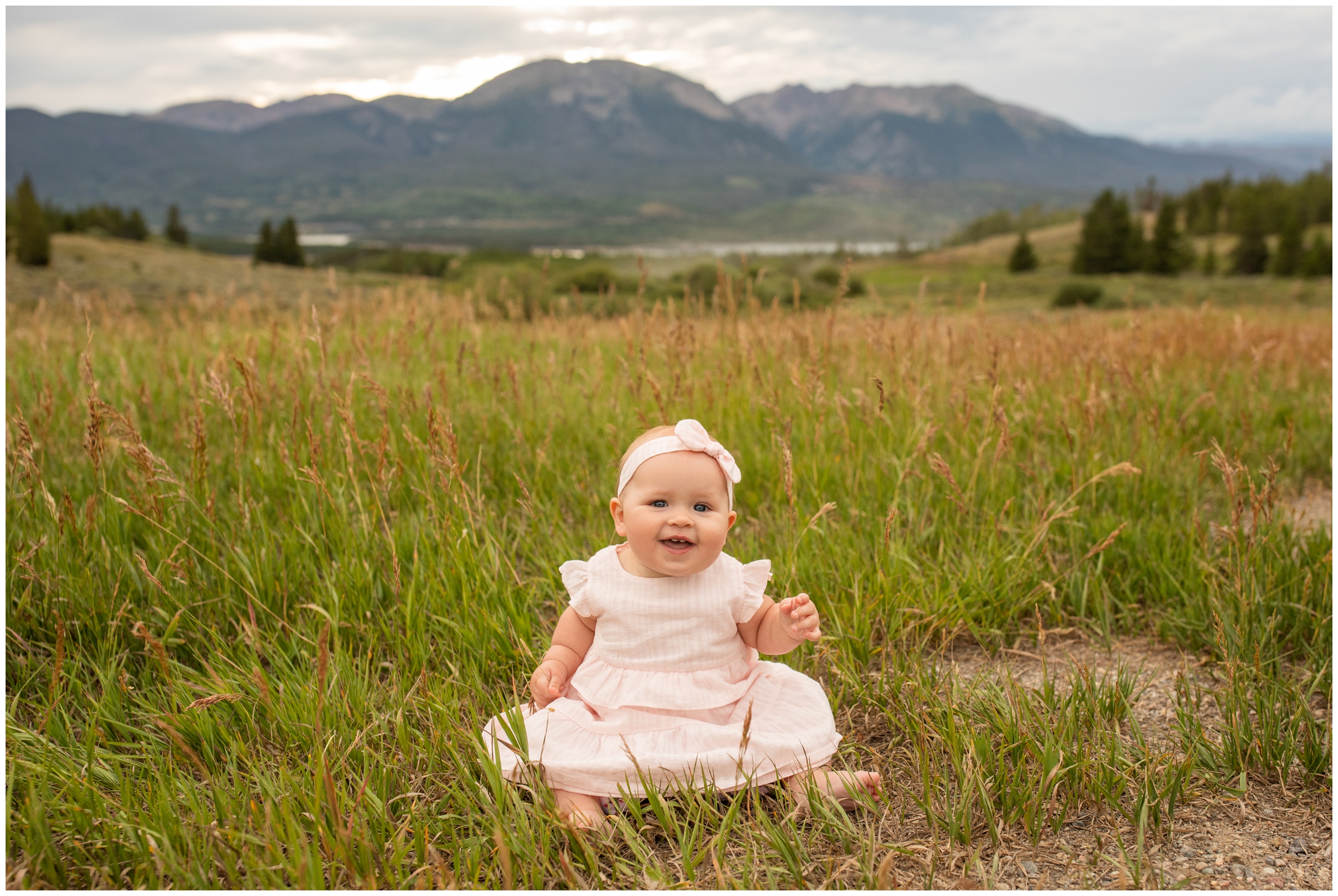 baby girl sitting in a field with mountain backdrop at Windy Point Campground in Summit County Colorado 