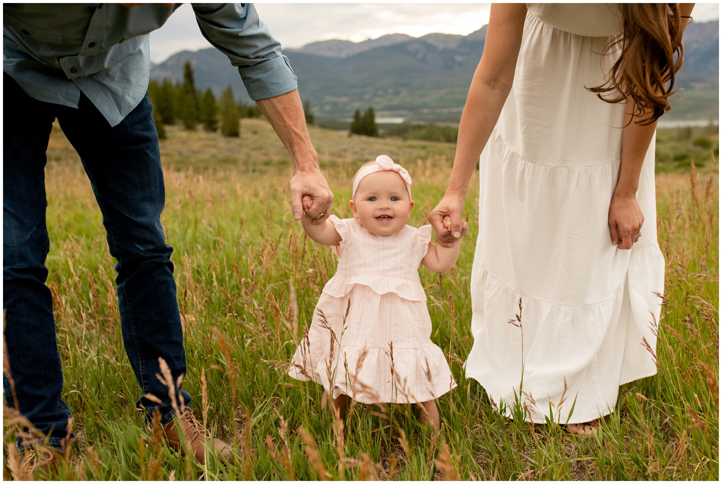 parents holding baby daughter's hands with mountains in background at Breckenridge Colorado family photography session 