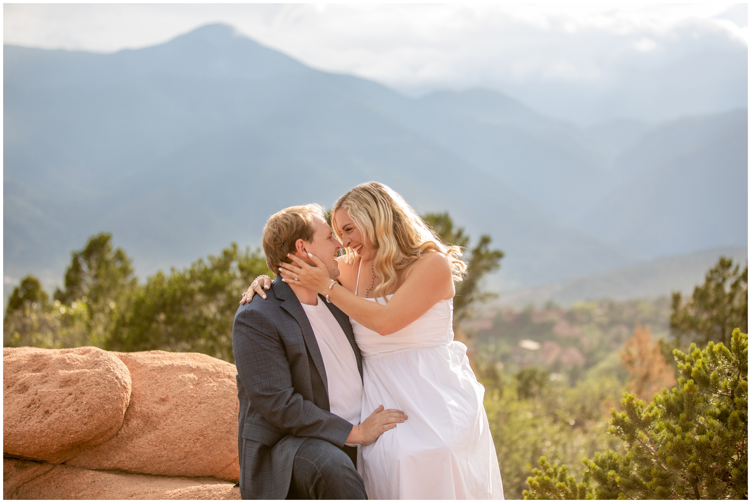 woman sitting on fiancé's lap with mountains in background during Colorado Springs couple's photos