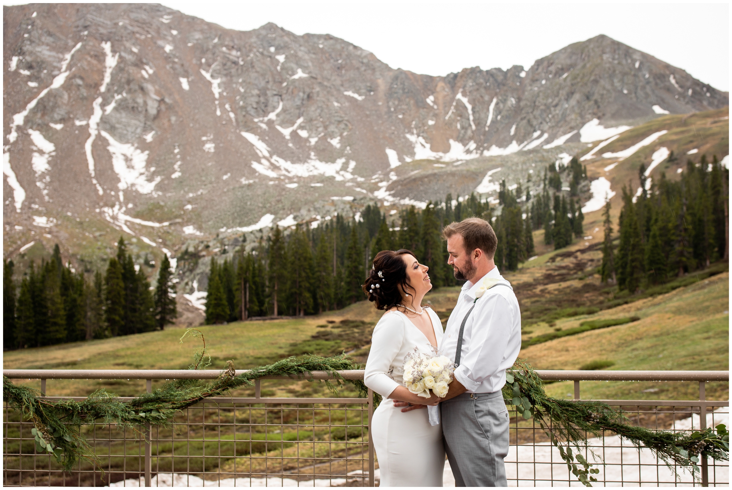 couple posing in front of mountains at Black Mountain Lodge during rainy Arapahoe Basin Colorado wedding pictures by Plum Pretty Photography