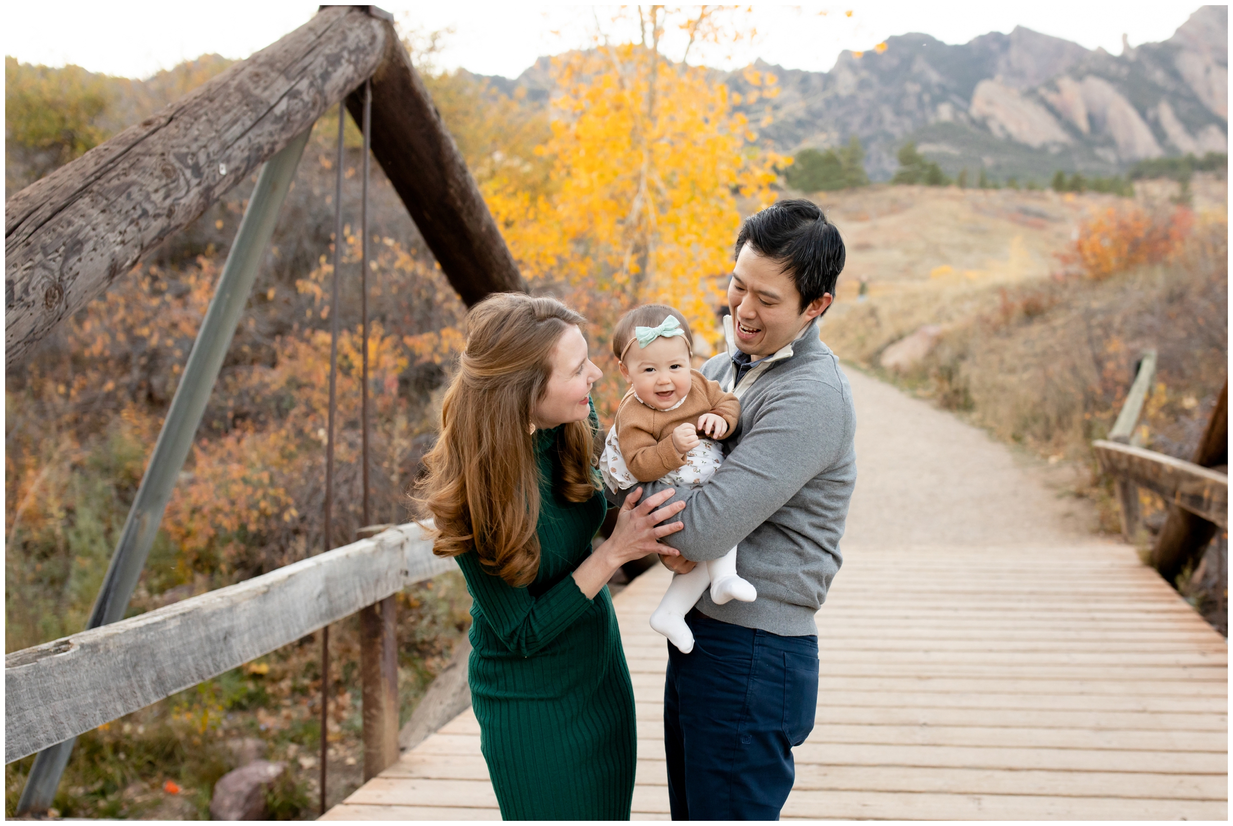 family posing on wooden bridge with fall foliage in background during Boulder Colorado family portraits 