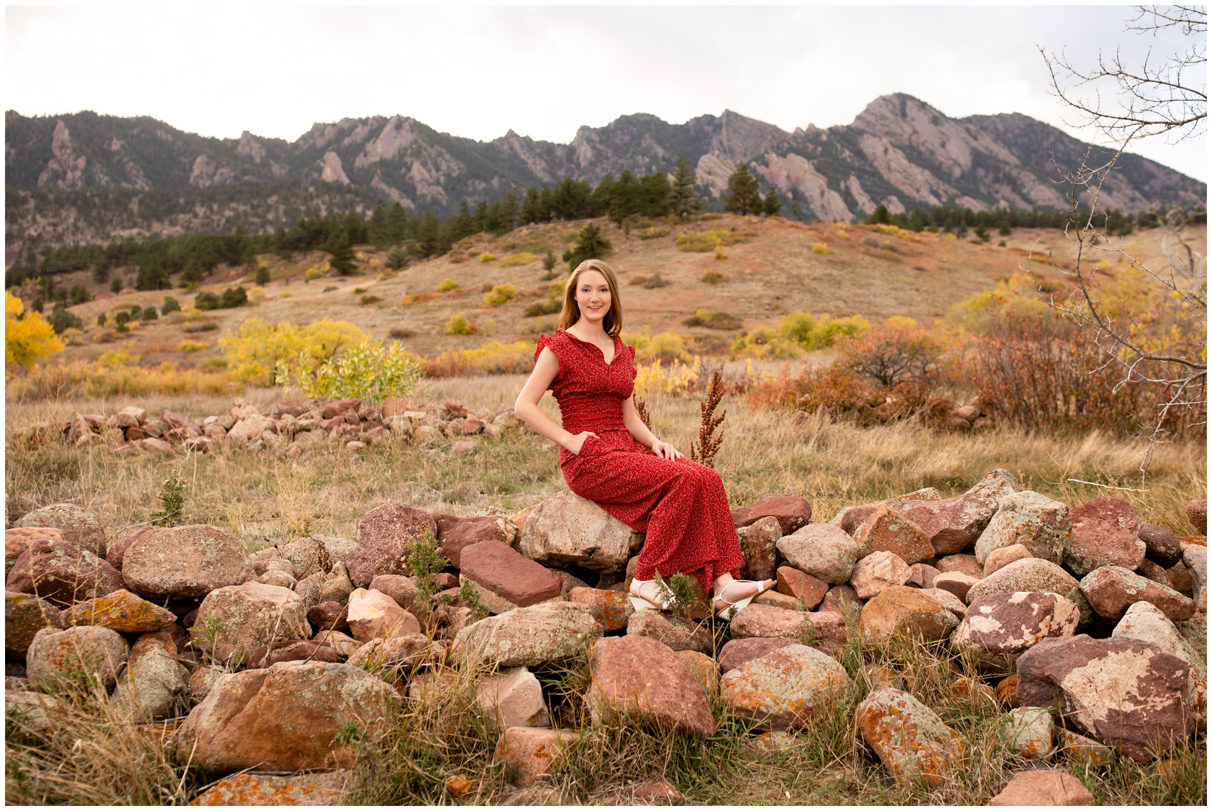 teen sitting on rock wall with mountains in background during Boulder Colorado senior photos