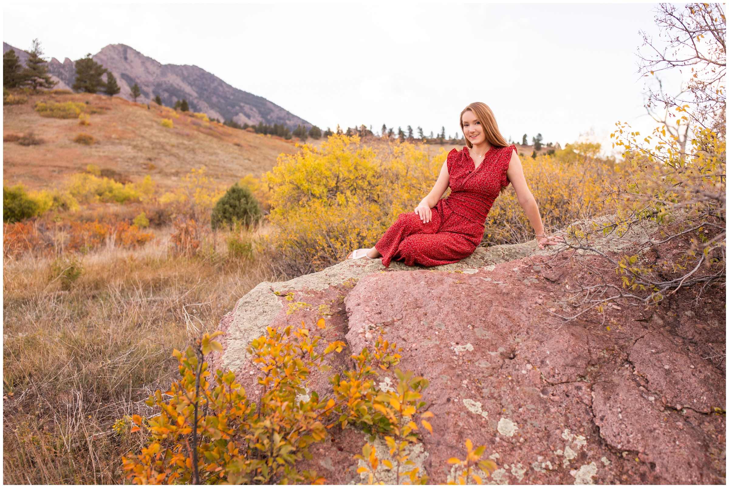 teen girl sitting on giant rock with Boulder flatirons in background 