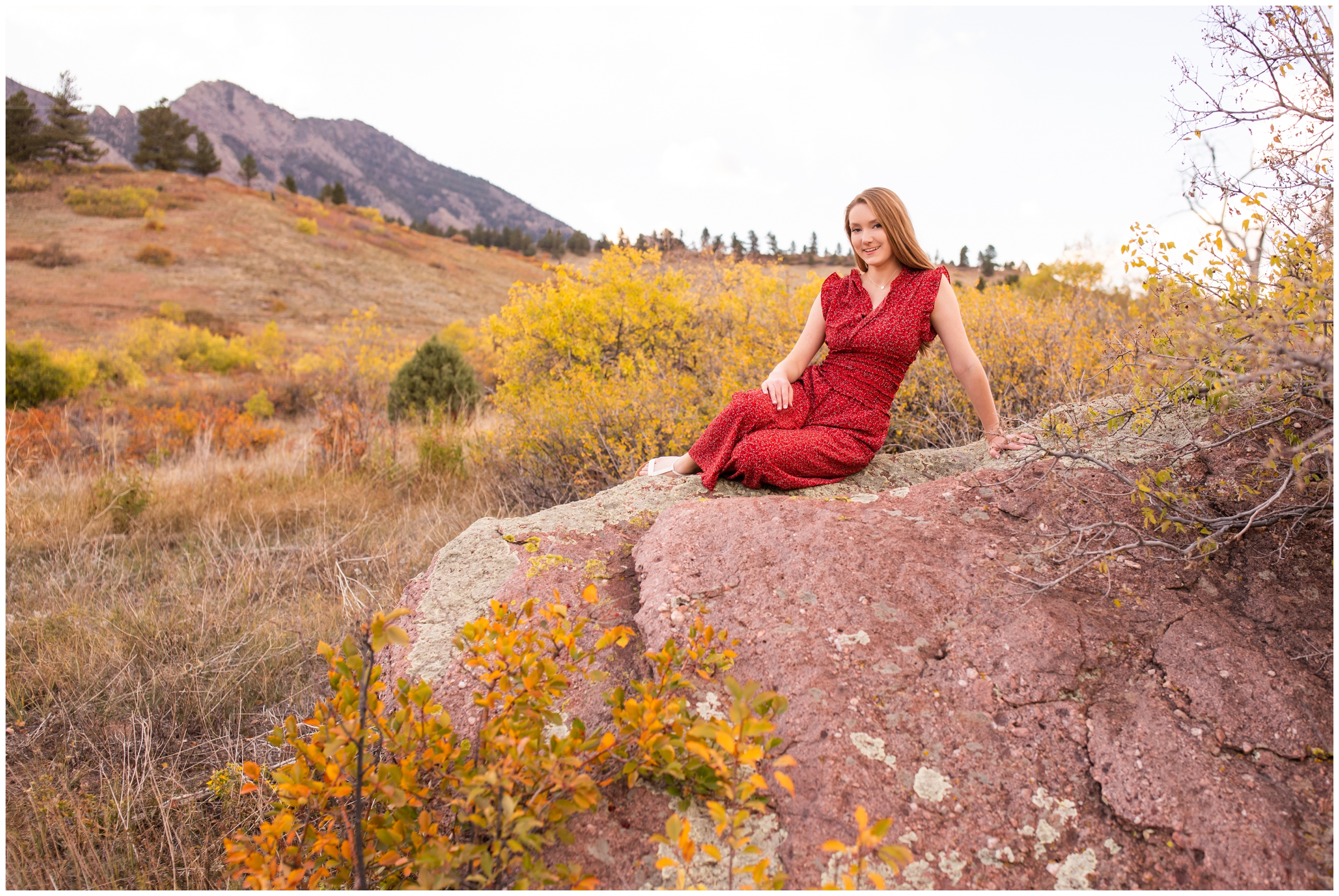 teen girl sitting on giant rock with Boulder flatirons in background