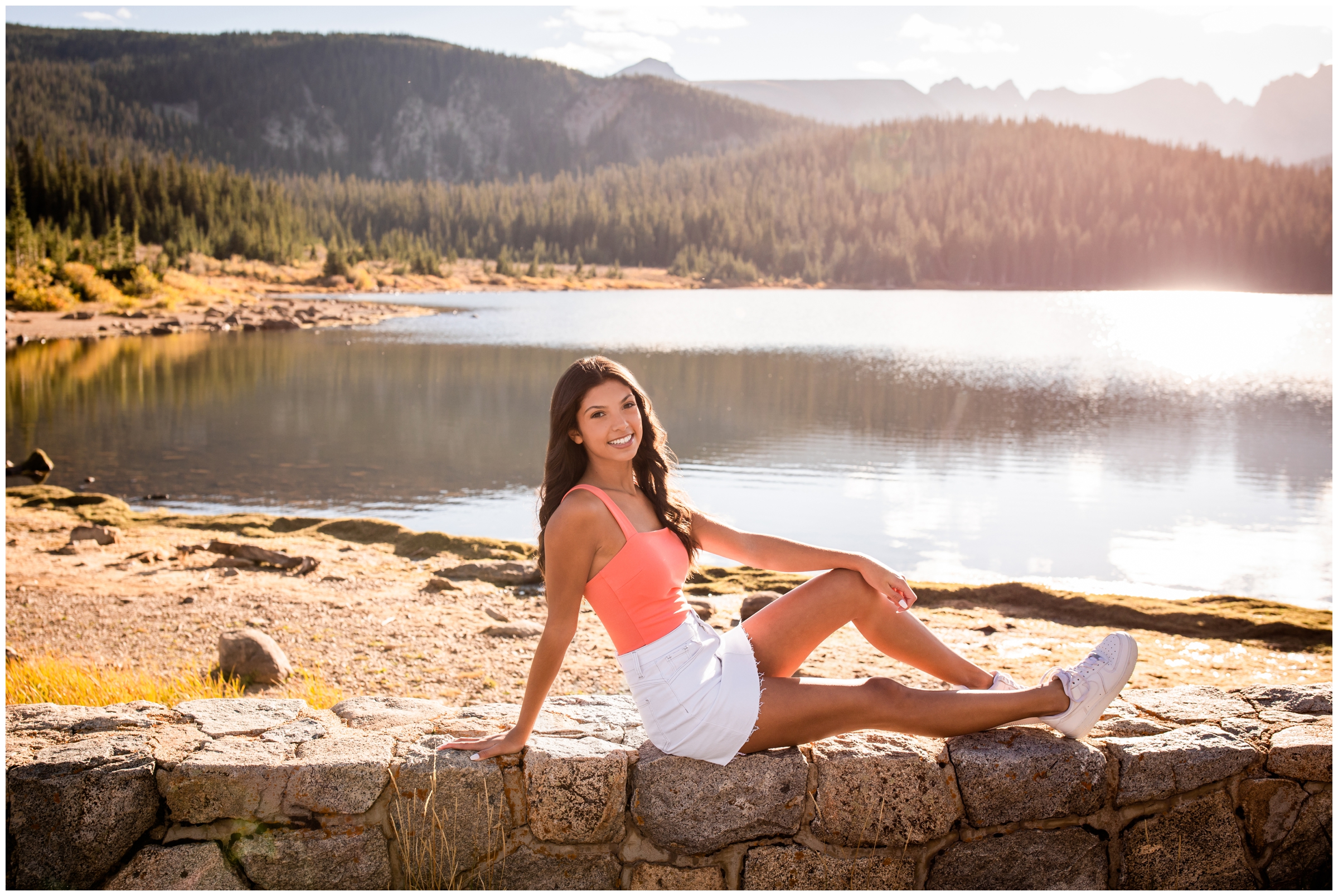 teen posing on stone wall with mountains and lake in background during fall senior pictures in Colorado 