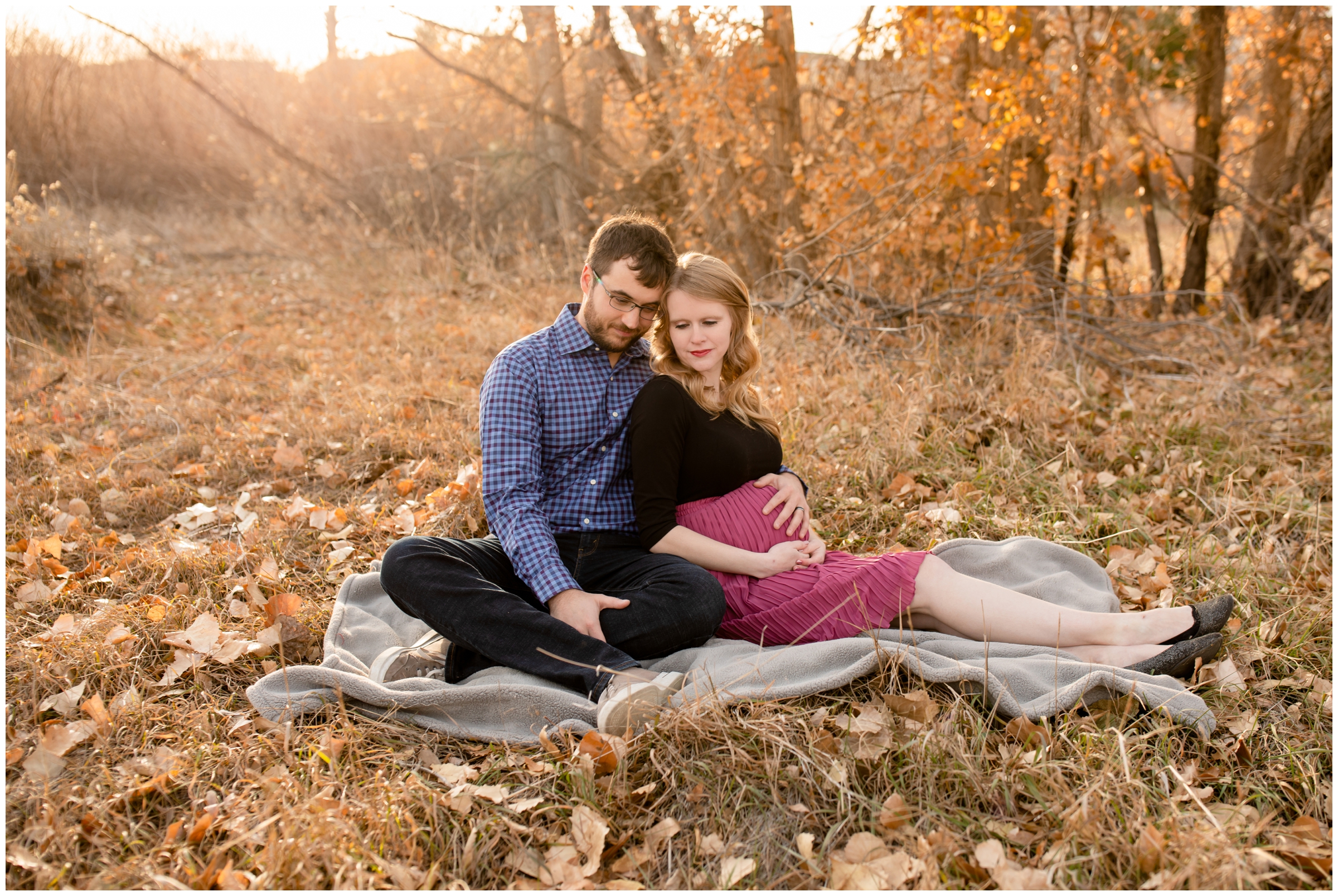 couple sitting in crunchy fall leaves during pregnancy photos in Centennial CO