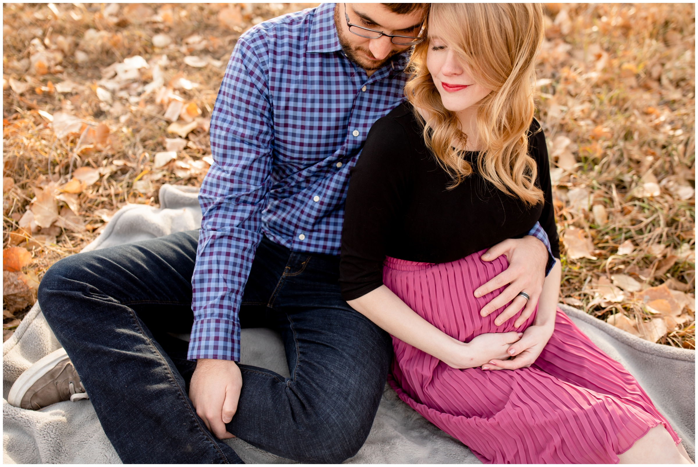 couple sitting in crunchy fall leaves during Centennial Colorado maternity photography session 