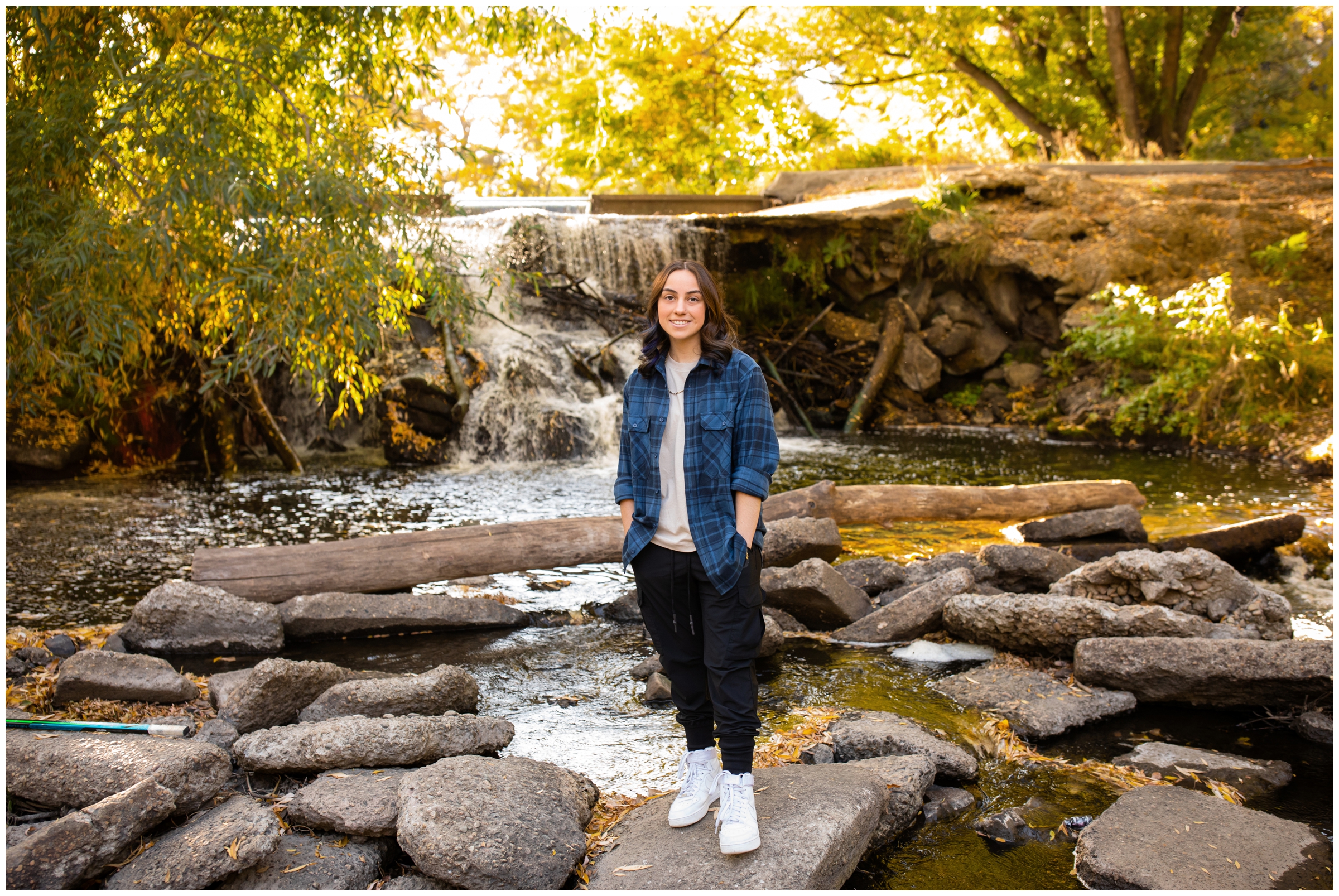 teen posing in front of waterfall with fall foliage in background at Mead High School Colorado senior photos