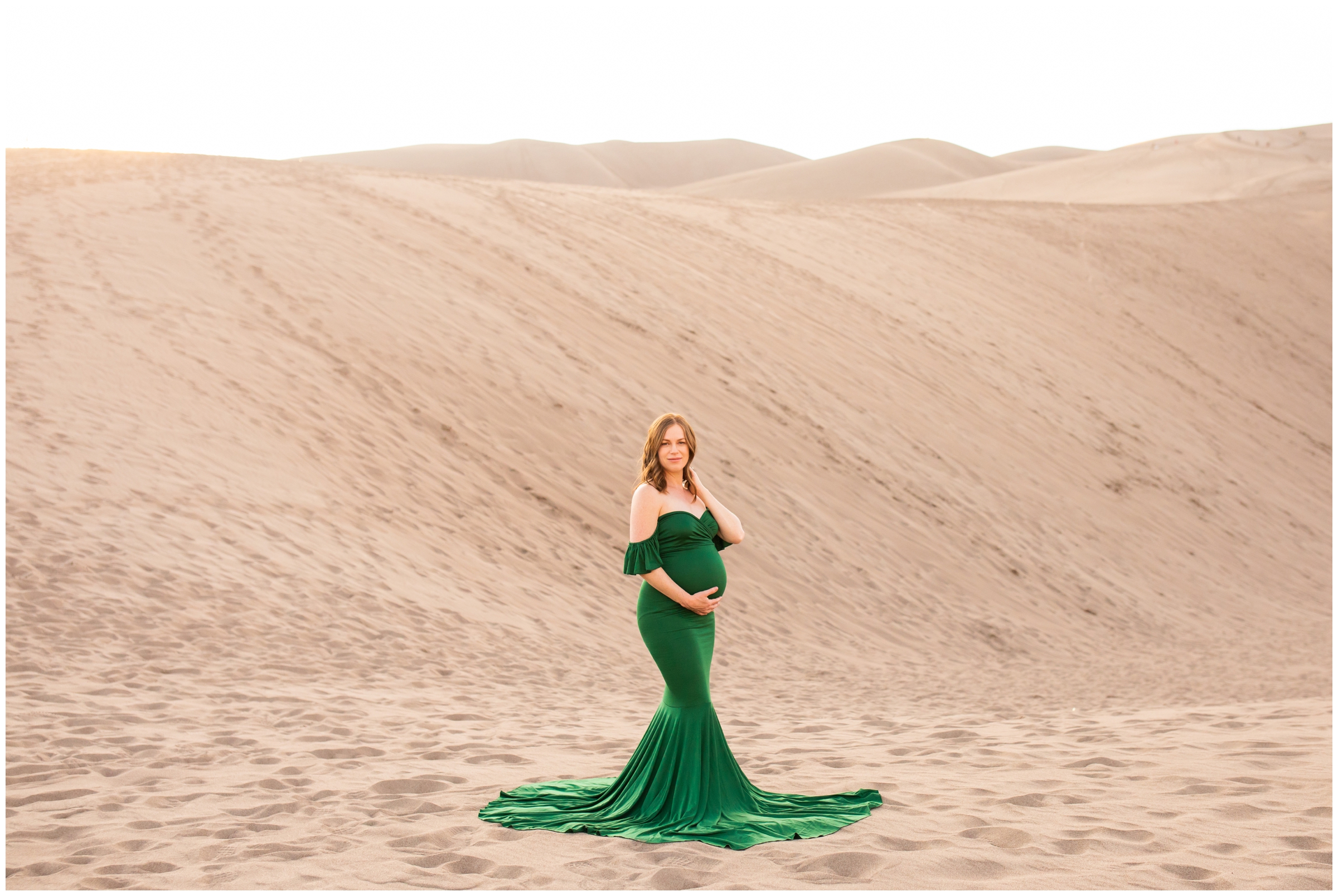 woman in a green maternity dress posing at the sand dunes in southern colorado during maternity photography session 