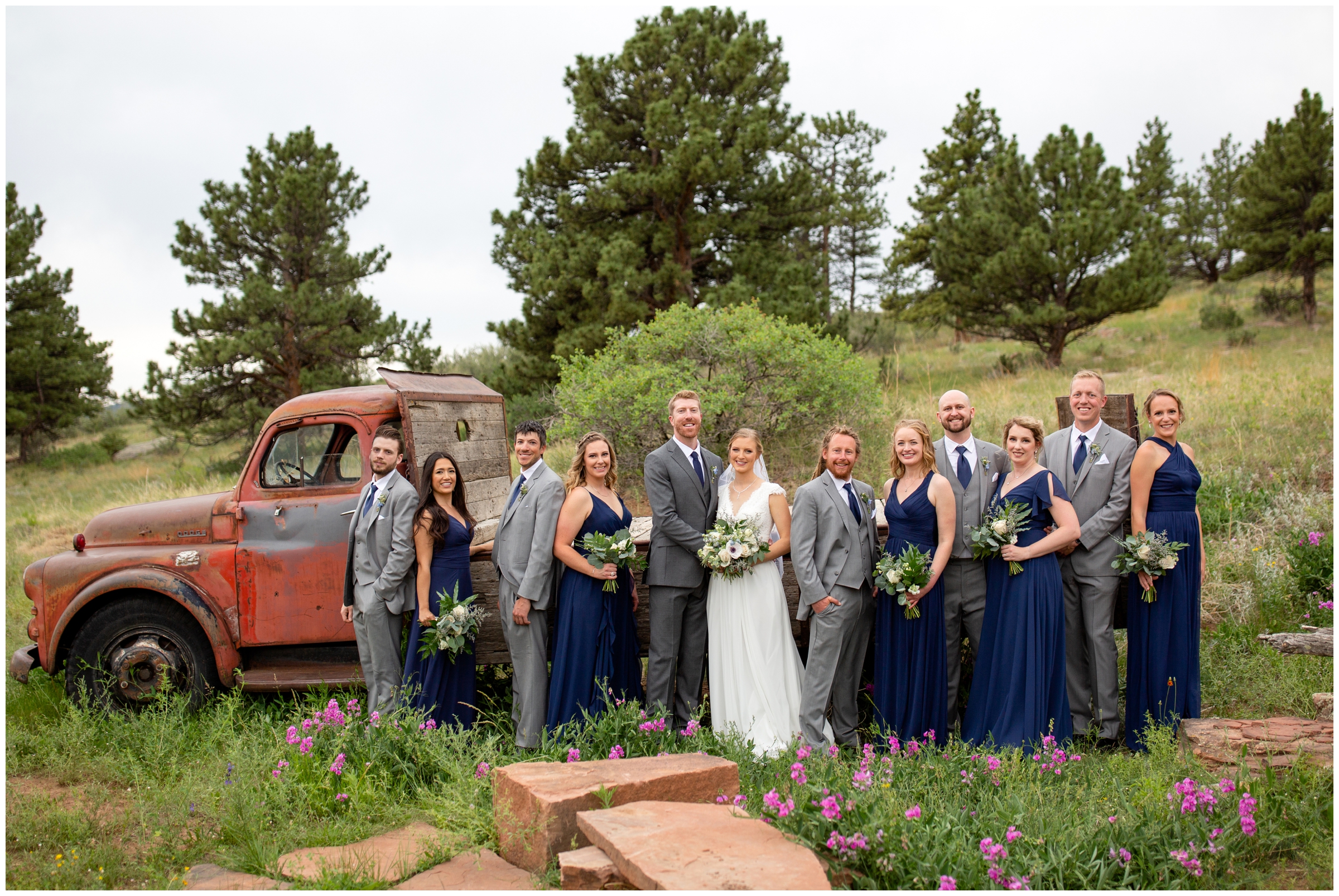 wedding party in navy blue and gray posing in front of vintage truck at Lionscrest Manor Colorado summer wedding 